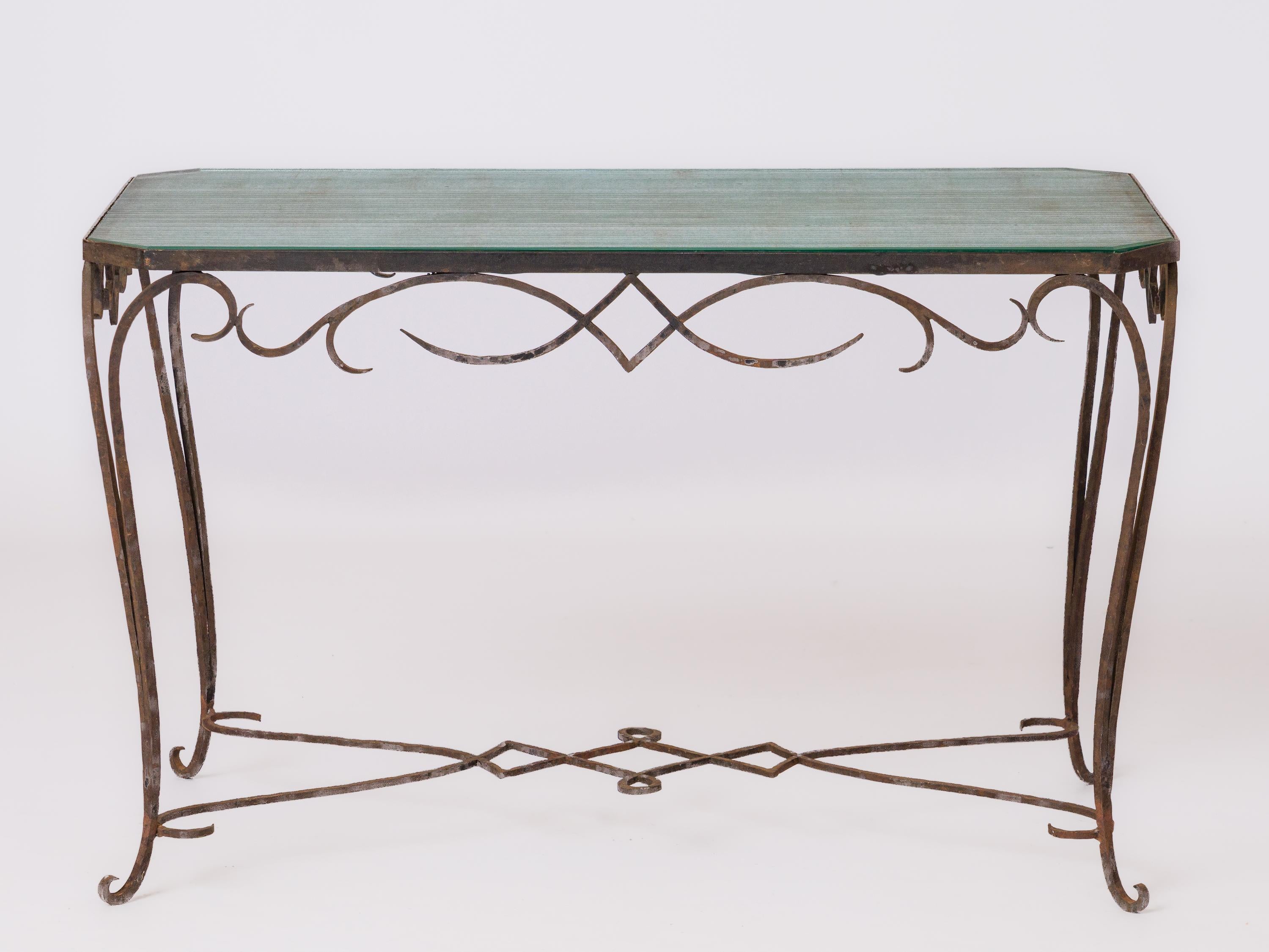 Table d'appoint en fer forgé à motifs de volutes et d'entrelacs attribuée à René Prou. Emblématique du début du style Art déco. Plan de travail en dalles opalines Saint Gobain à pans coupés.
Petites bosses et ébréchures au dos de la dalle. Traces de