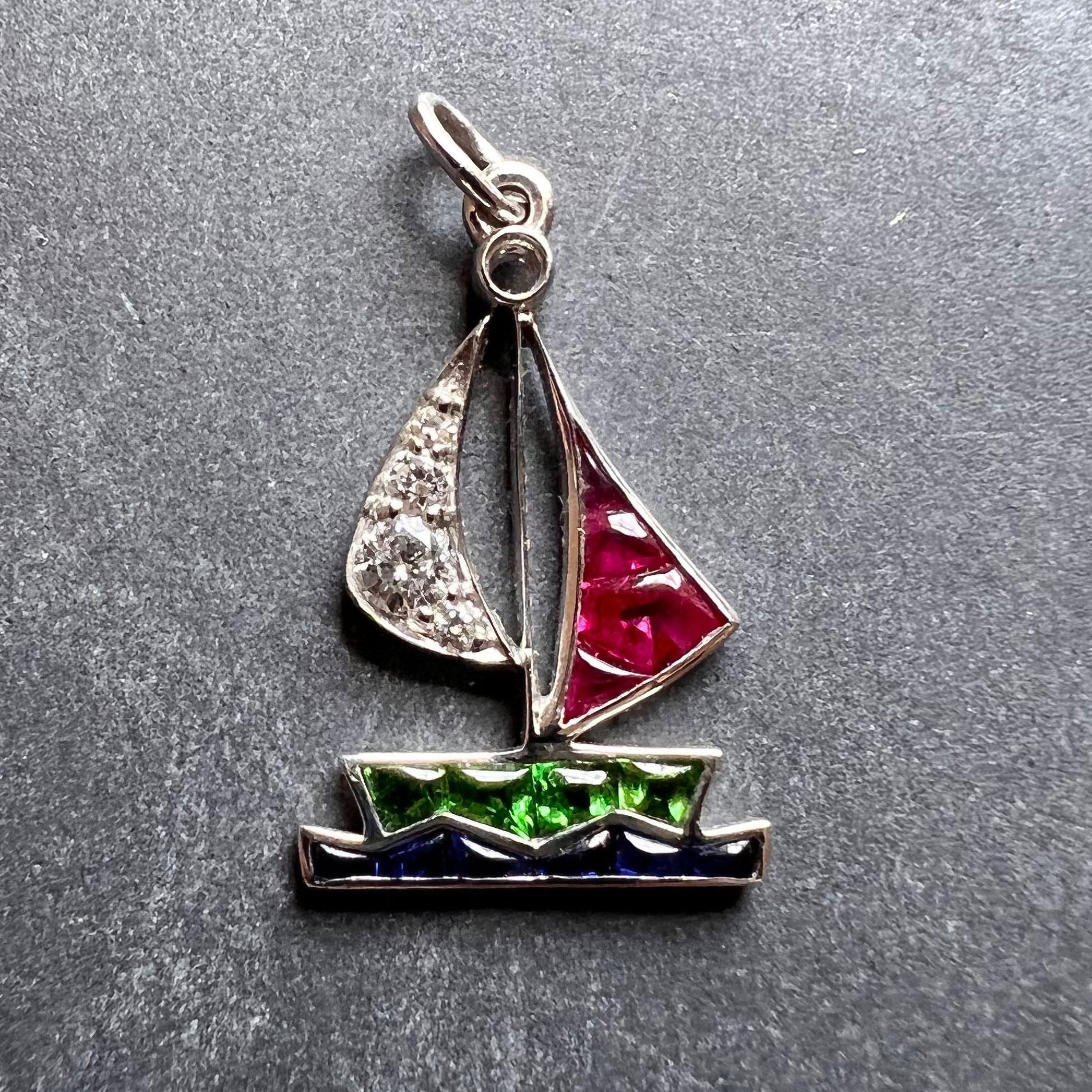 An Art Deco platinum charm pendant designed as a peridot sailboat with ruby and diamond sails on a sapphire set sea. The charm is set with four round brilliant cut diamonds, four buff-top rubies, six buff-top sapphires and four buff-top peridots.