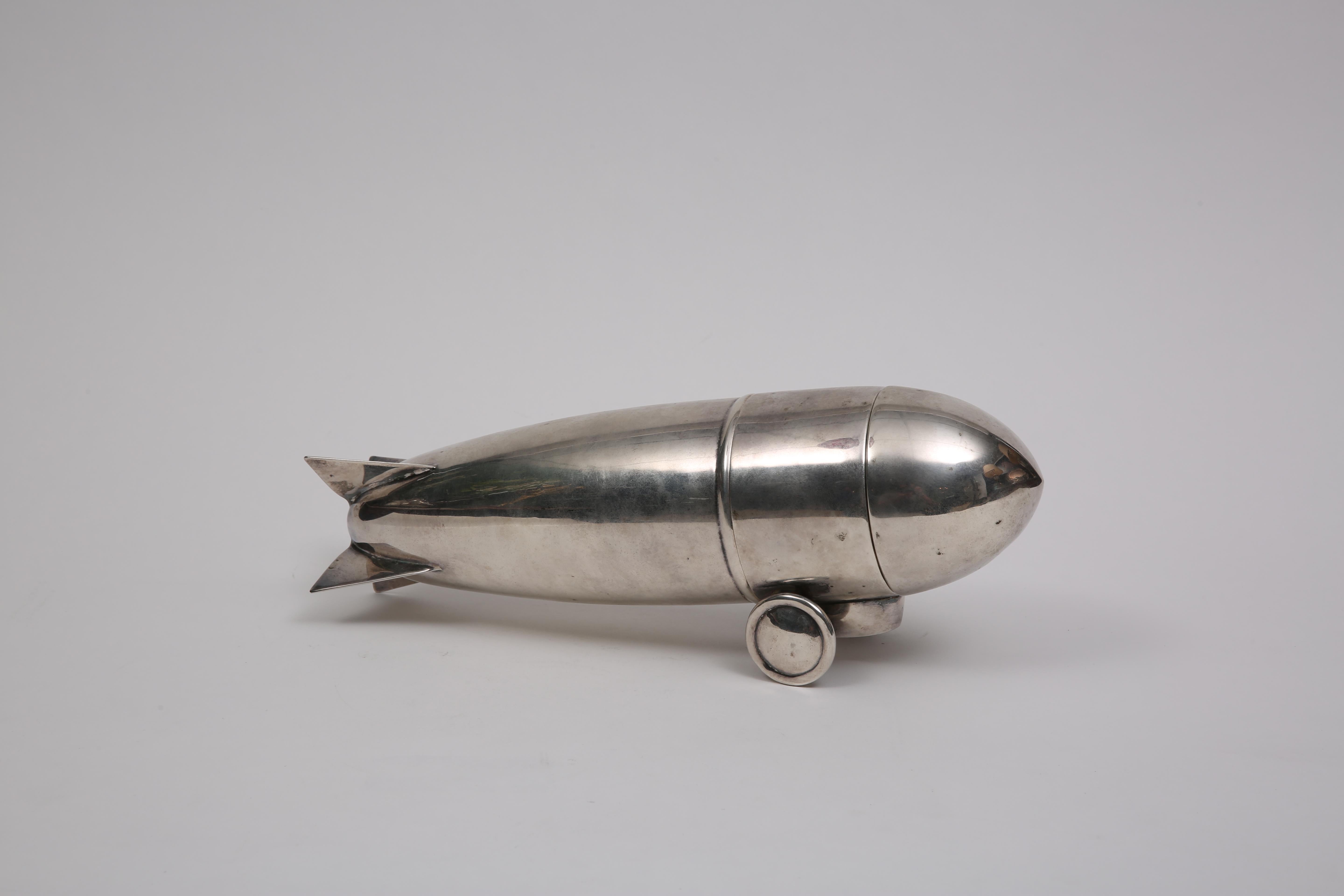 This piece was designed to be a traveling cocktail bar in the shape of the Zeppelin Airship. It is very rare and in pristine condition. Its silver plated brass in material and has an integral strainer with a removable lid, and cap. This piece is