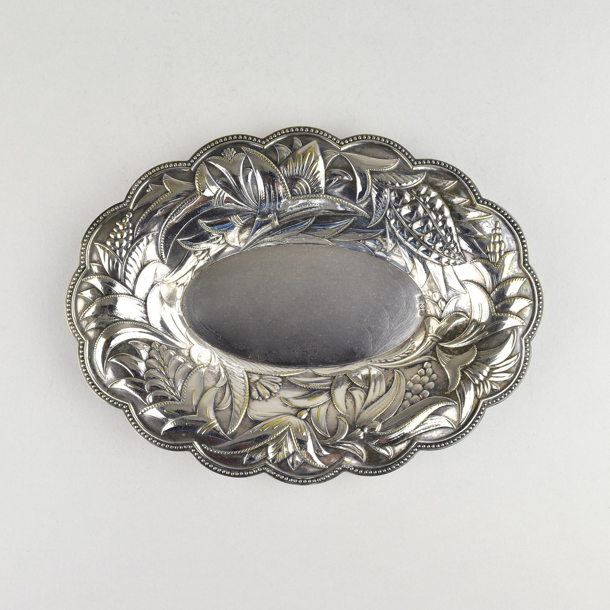 Élégant plat fourre-tout Art déco en métal argenté de WMF, finement travaillé dans le style Wiener Werkstätte. La pièce présente un bord joliment festonné et des motifs floraux et feuillus richement gaufrés entourant un centre ovale lisse, ce qui la