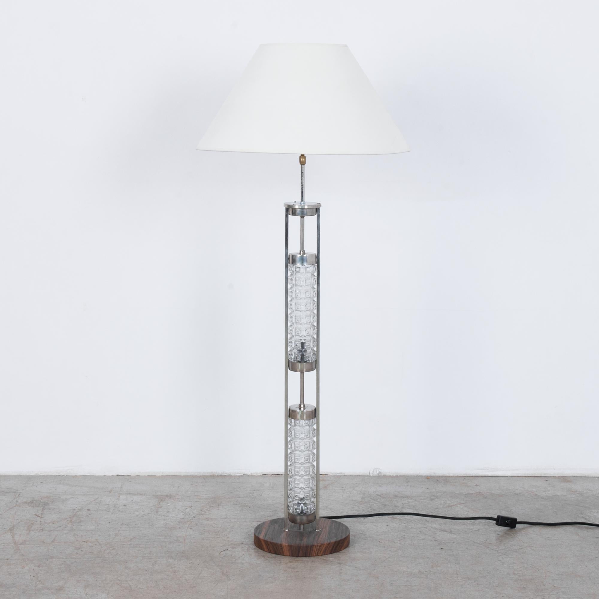 A chrome-plated brass floor lamp from Germany, circa 1960. Two cylinders of patterned glass sit within a silver metal frame, creating a linear silhouette. A natural white shade complements the modern geometry. A serene and stylish piece, fully