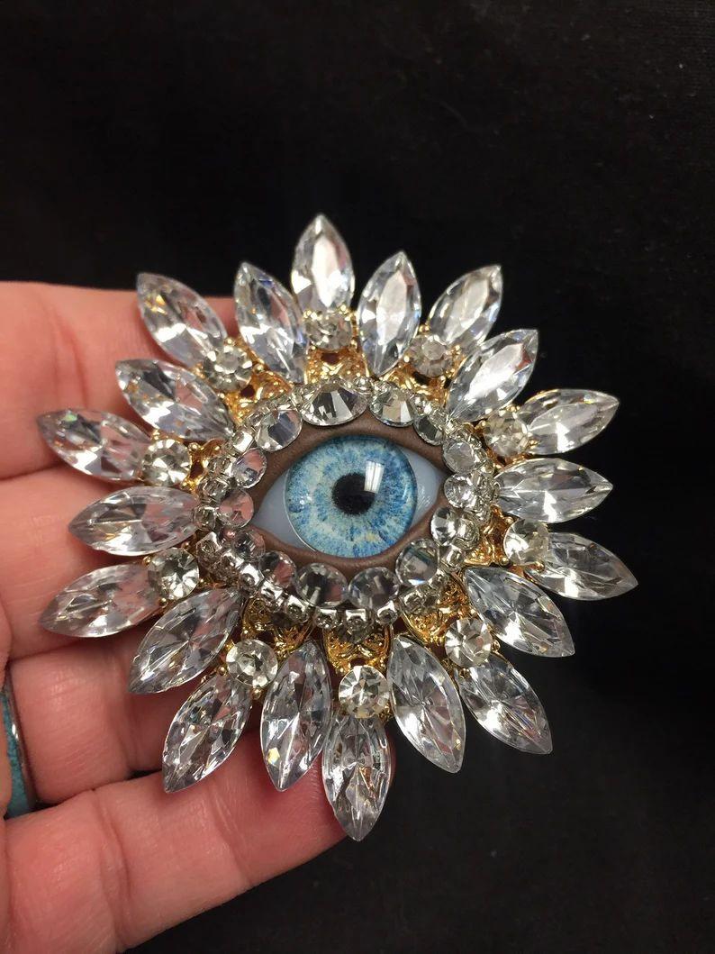Einfach schön! Art Glass Evil Eye Crystal Golden Vintage Mid Century Modern Statement Brosche Pin Zentrierung eines Art Glass Evil Eye. Umgeben von handgesetzten goldenen Marquise-Kristallen im Sunburst-Design. Ungefähr 3