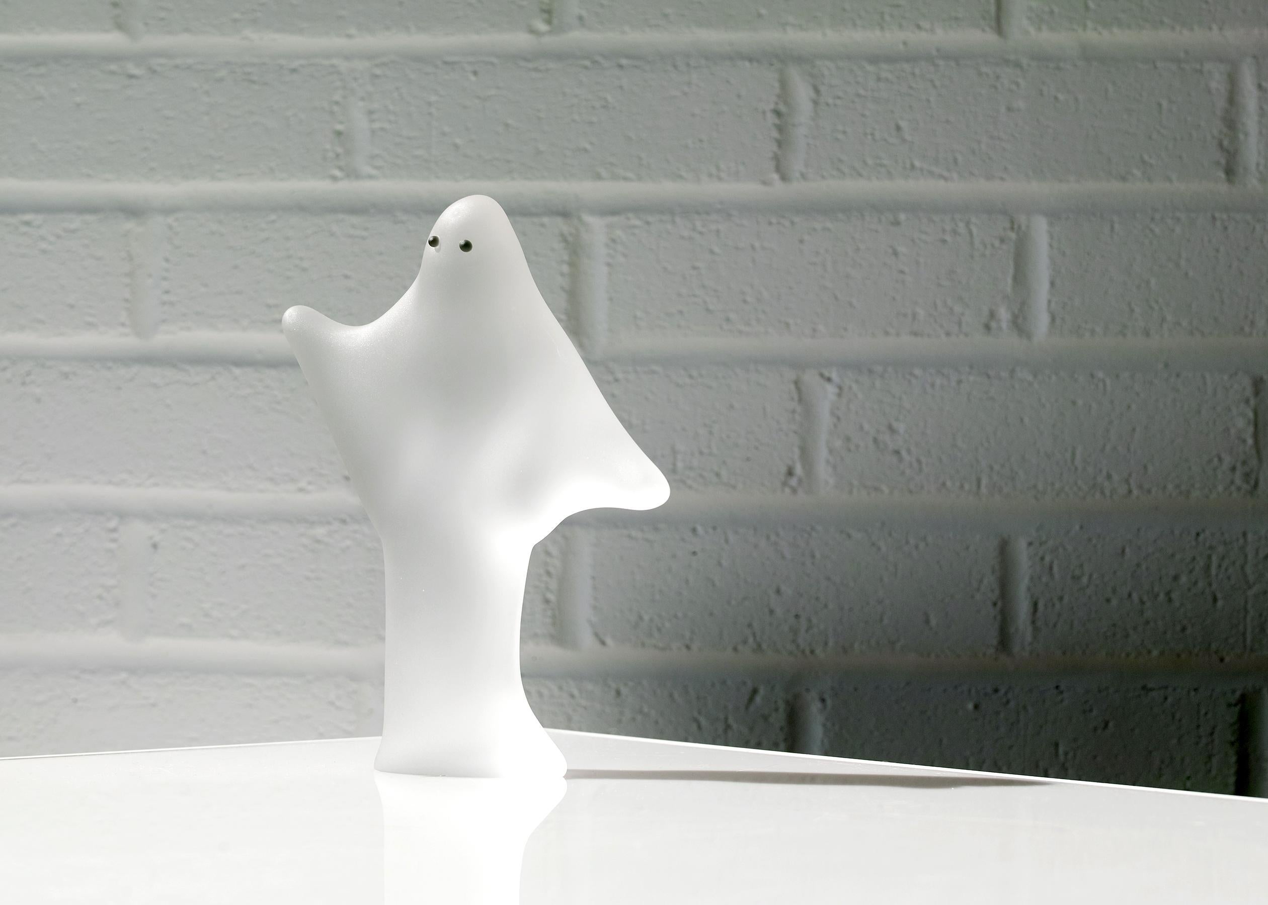 For your consideration is this art glass ghost sculpture with a soft satin surface, gently rendered contours, and one sold piece of glass for the body with two black beads for eyes. The ghost appears in movement with arms raised and the drapery of