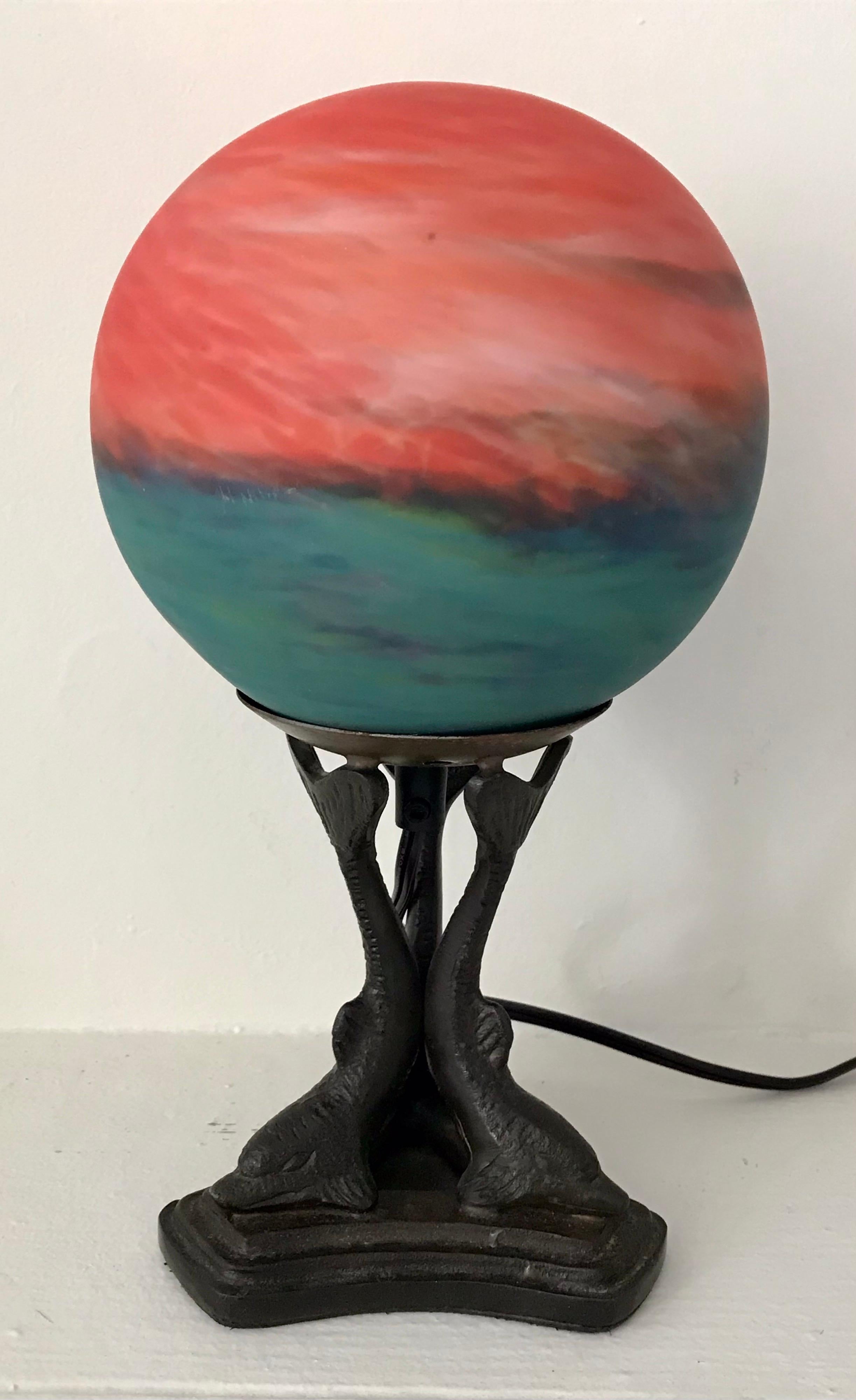 Beautiful colorful art glass globe table lamp mounted on cast metal dolphin base, 20th century, rewired with inline switch.