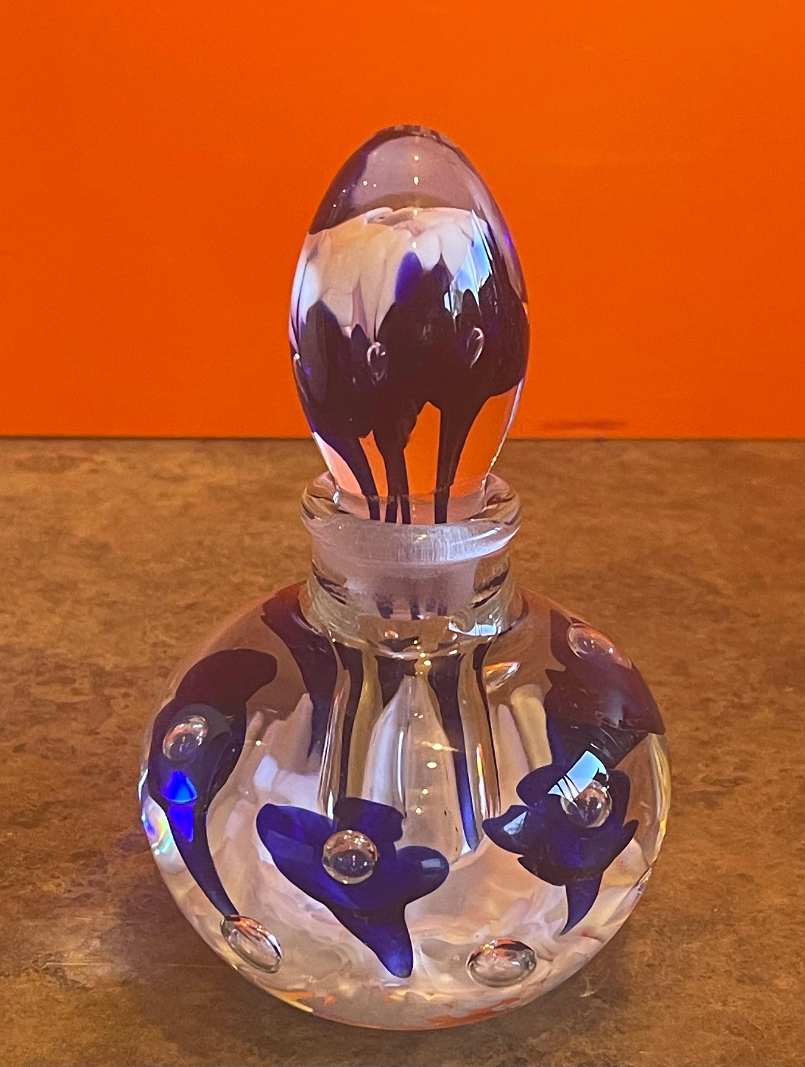 Beautiful art glass perfume bottle by Joe Rice, circa 1990s. The bottle is clear glass with white petals on the bottom and bright blue flowers floating in the glass. The piece is in very good condition with no cracks or chips and measures 3.75