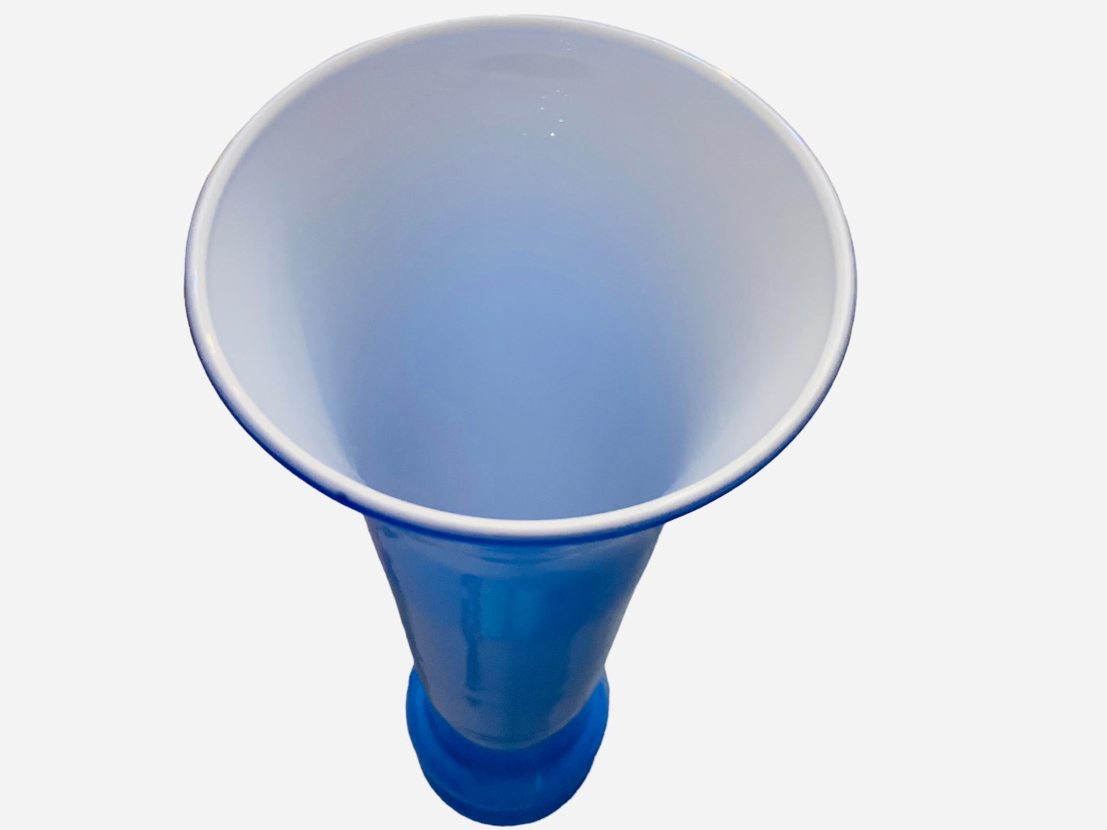 This is an Art Glass royal blue and white glass vase. It depicts a tall fluted royal blue glass base adorned with two rings made of the same glass in the lower body of the base. The inside of the vase is white. The vase is attached to a round clear