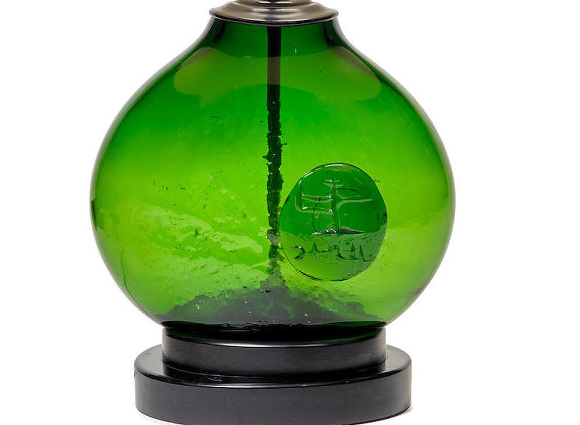 A blown art glass lamp Model 551 by Wayne Husted for Blenko 1970s. Made with his signature techniques, the bulbous body of a dark green color features a prominent molded medallion on the front and scattered dimple surface texture for visual delight.