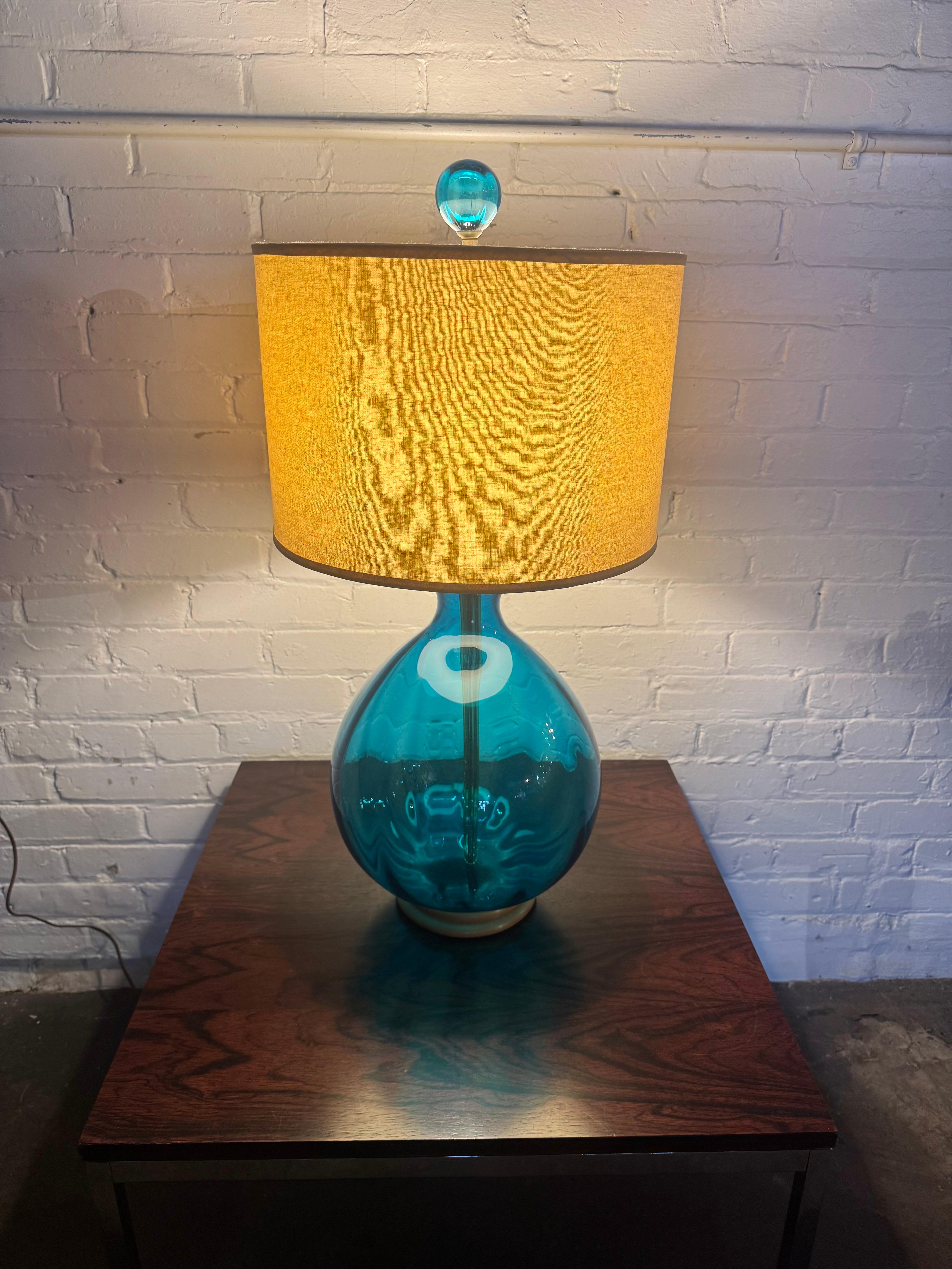 A blown art glass lamp Model 551 by Wayne Husted for Blenko 1960s. Made with his signature techniques, the bulbous body of a teal blue color features a prominent molded medallion on the front and scattered dimple surface texture for visual delight.