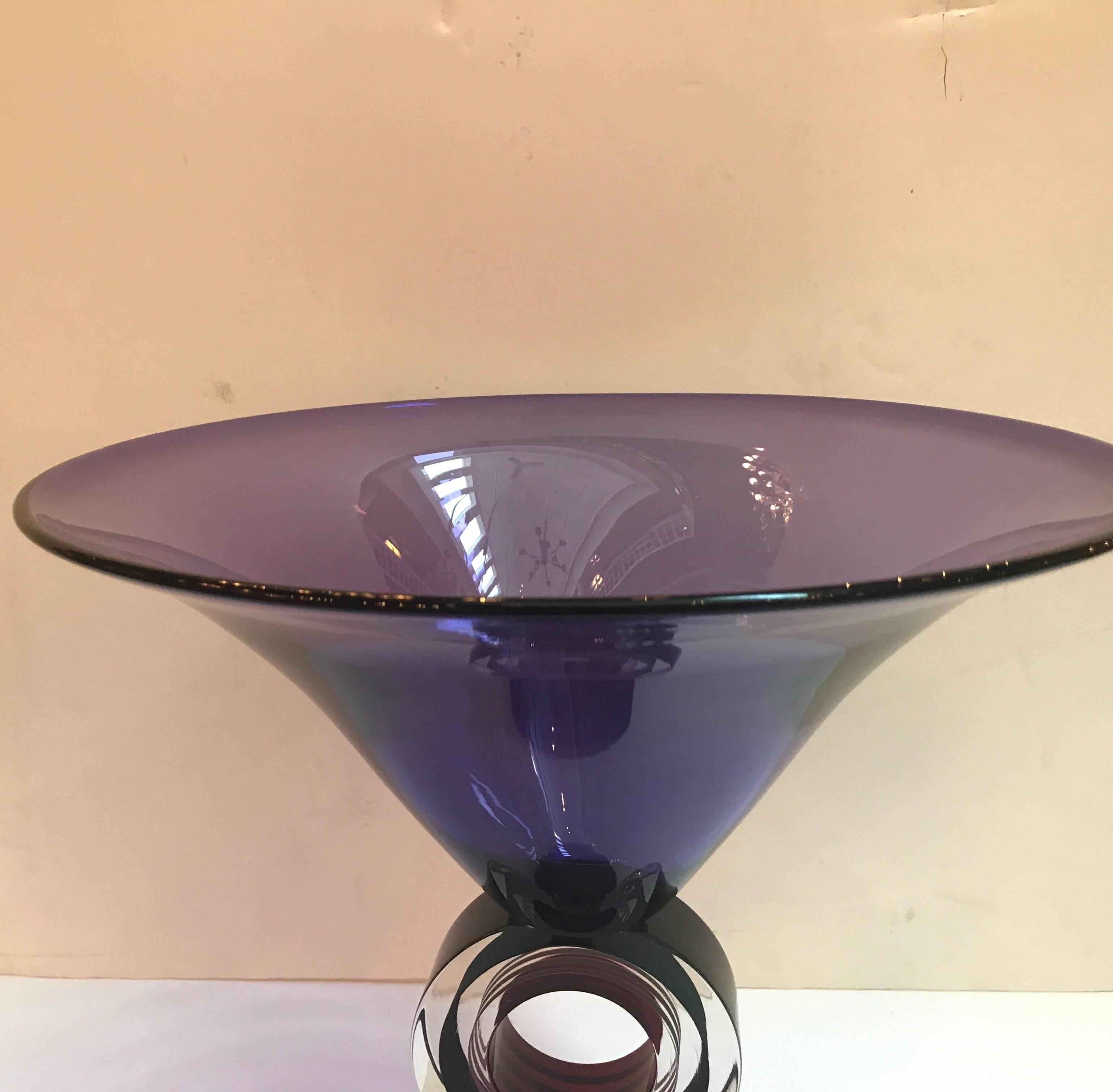 A tall modern trumpet form center bowl with unusual pedestal base. The base with a circular stem with bands of colored glass resting on a black solid glass cone base. The piece is signed and numbered limited edition of 500. The artist signature is