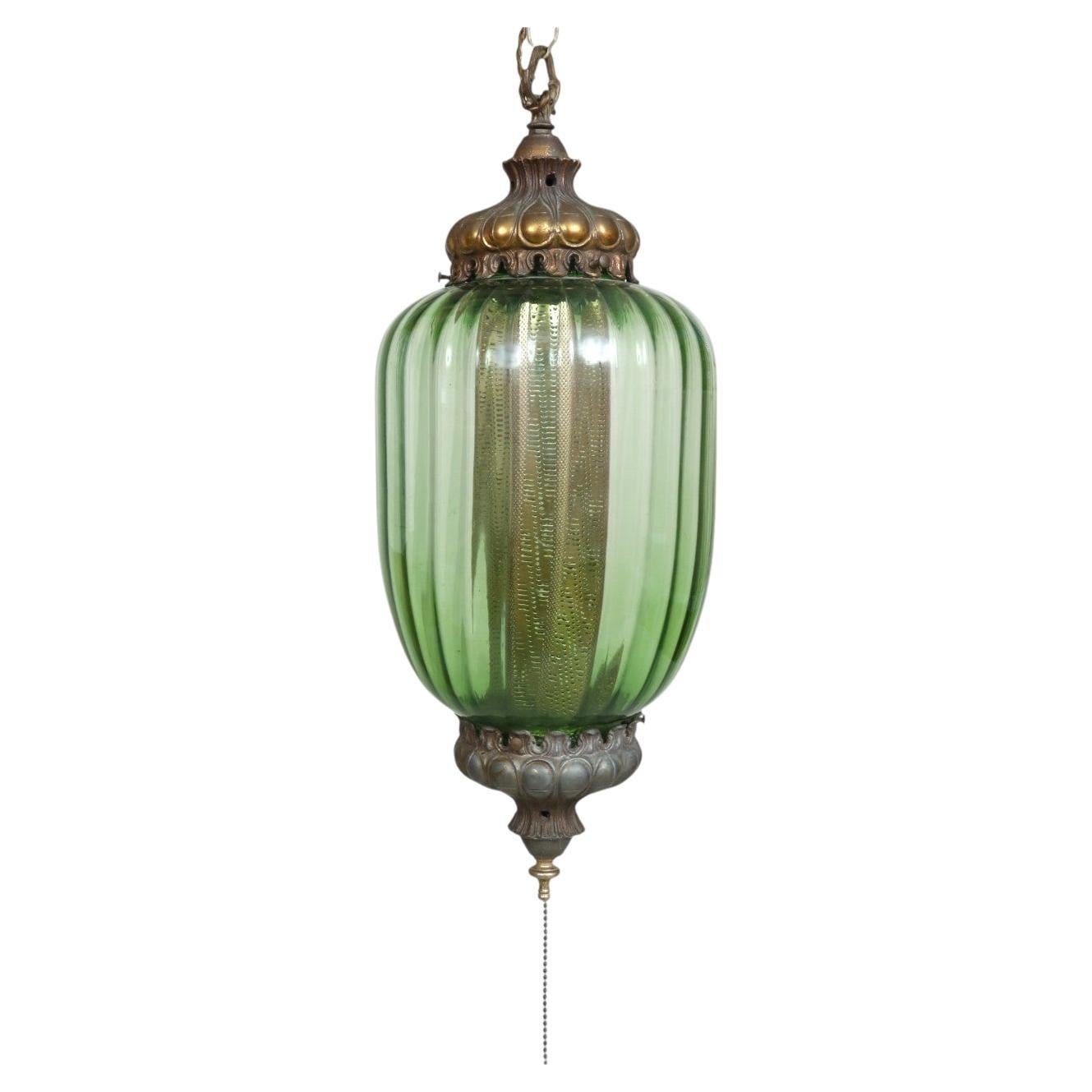 A pair of Art Moderne glass lanterns, circa 1940s. Kelly green ribbed glass lanterns are secured with cast metal caps and switch on with pull chains from below. Lanterns hang with accompanying chains. Dimensions do not include chain or pull chain. 