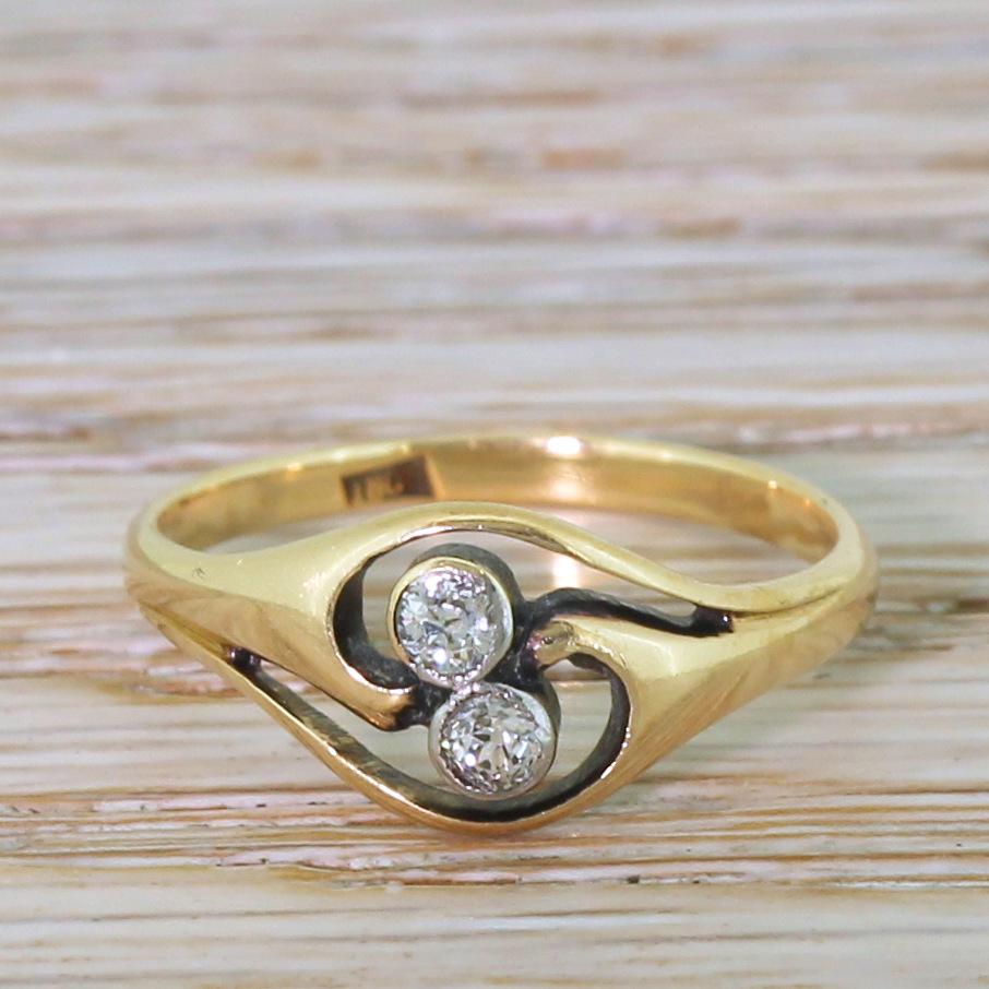 A wonderfully elegant Edwardian diamond ring. A pair of bright old mine cut diamonds are rubover set and sit within a wonderfully elegant and sweeping crossover setting. Sits nice and close the to finger, making this ring practical as well as