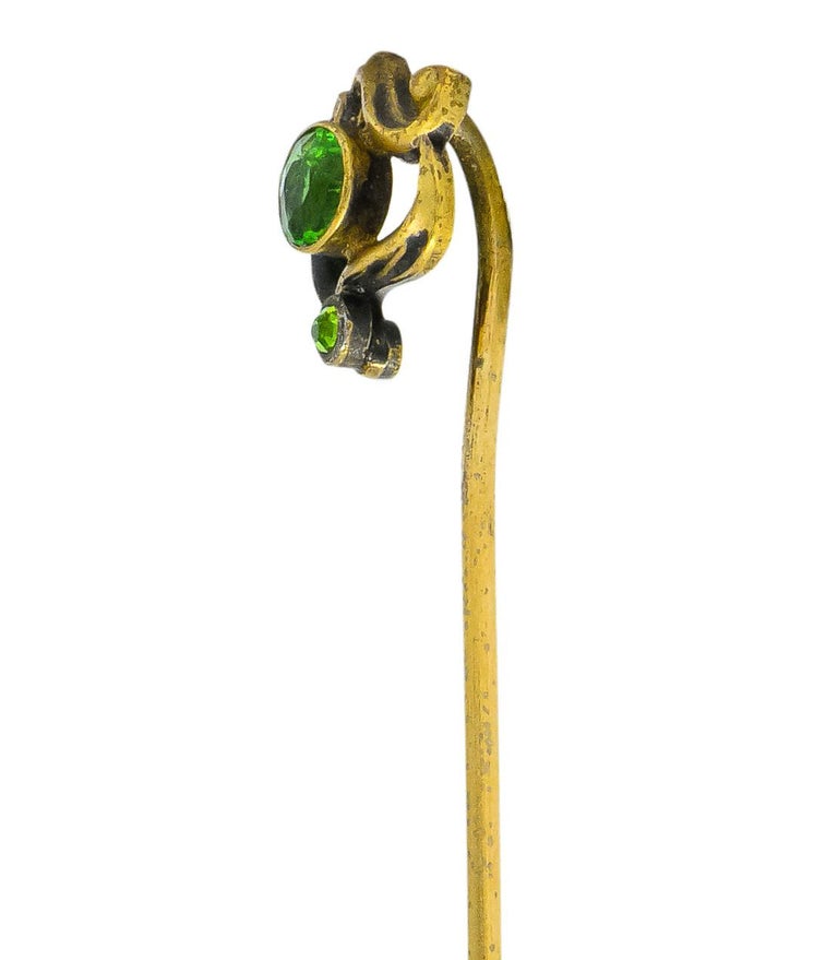 Centering two bezel set round and old European cut demantoid garnets weighing approximately 0.40 carat total, transparent medium-dark yellowish-green

Surrounded by three sections of swirling Art Nouveau whiplash

Tested as low karat gold

Top