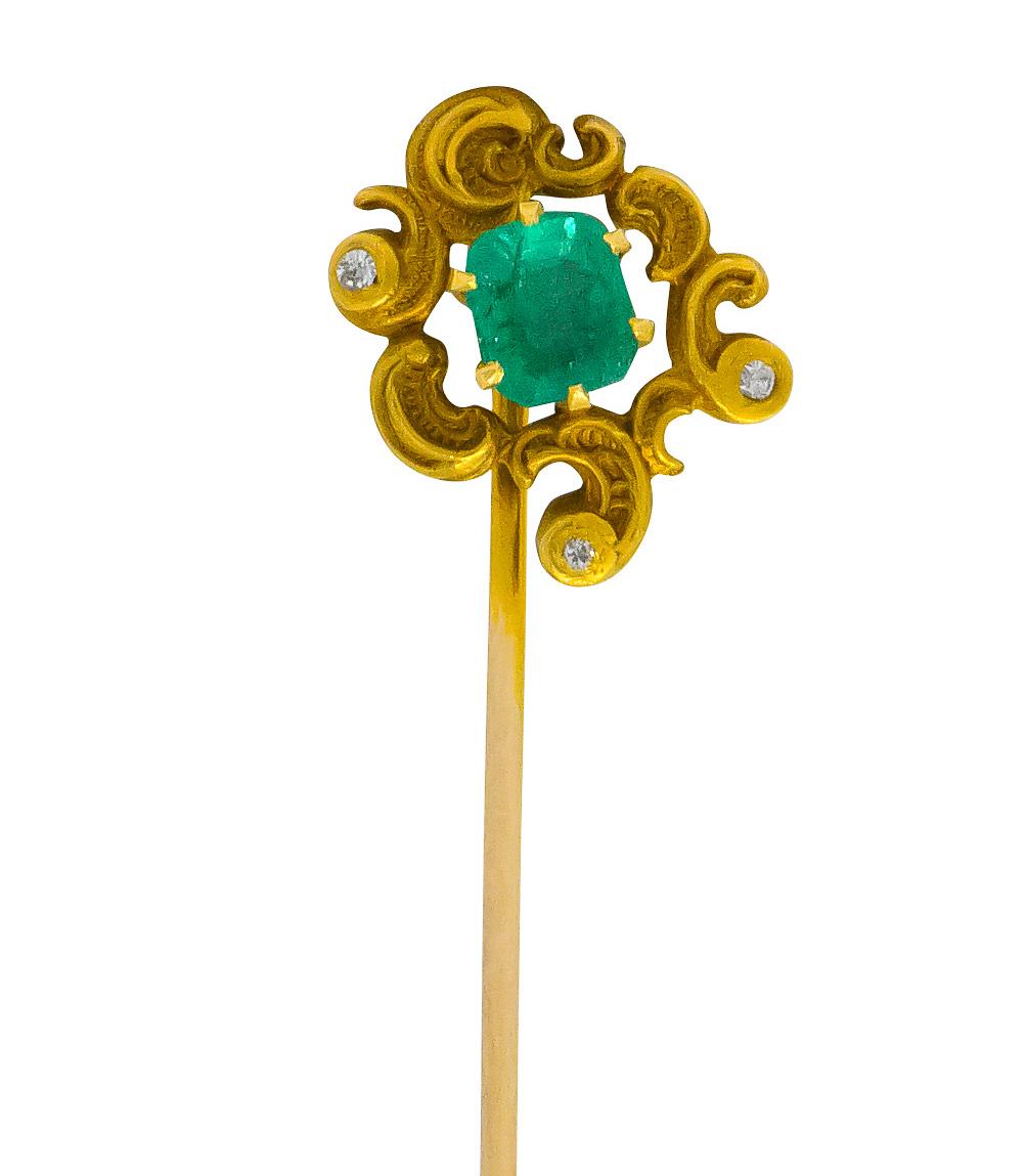 Centering a claw set rectangular step cut emerald weighing approximately 0.58 carat, translucent lush bluish-green

Accented by three bezel set single cut diamonds with remaining weight

Surrounded by matte gold paisley style whiplash with deeply