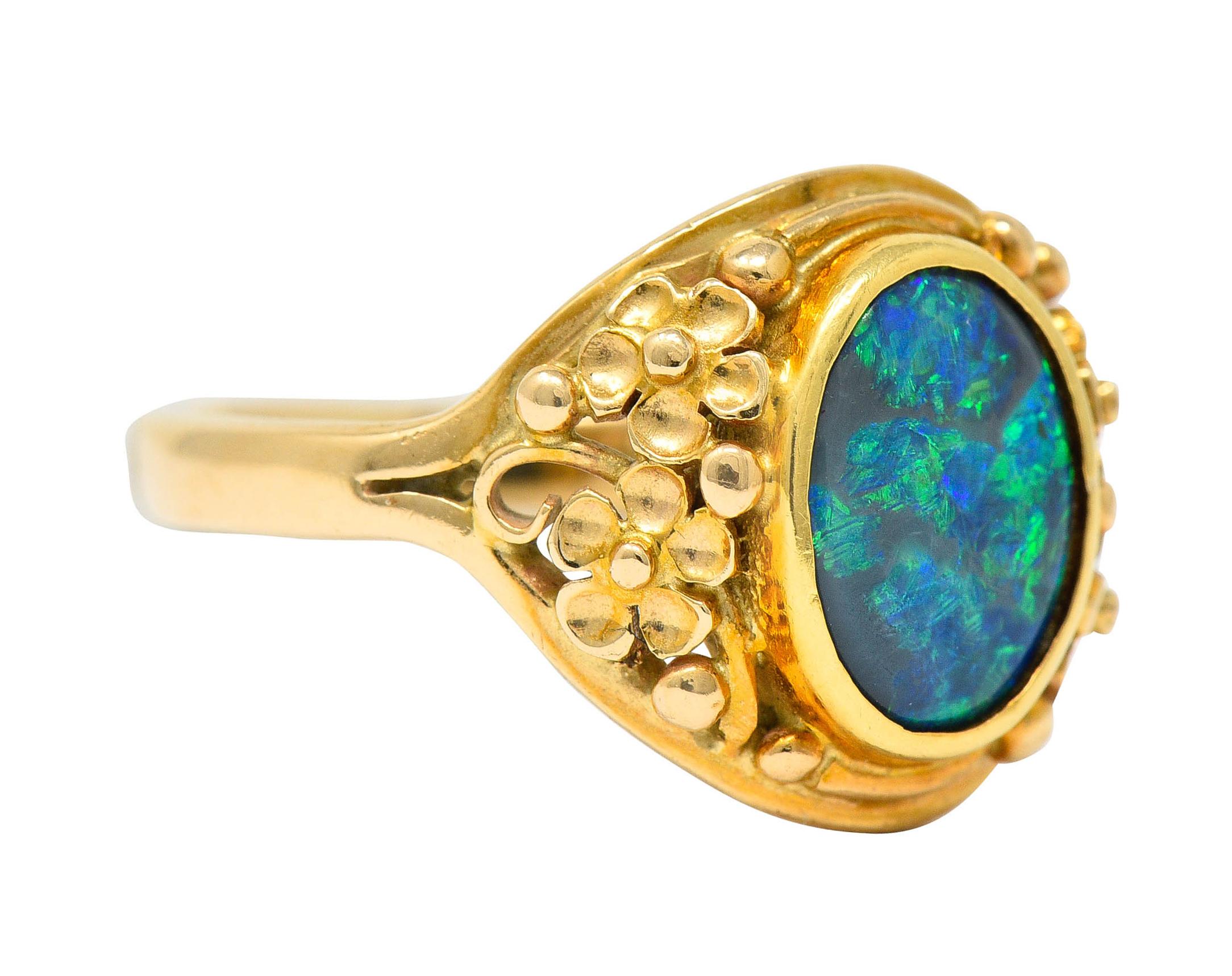 Centering a bezel set black opal cabochon

With vivid play of color and measuring 8.5mm x 6.5mm

Set within a 14 karat gold mount and flanked by floral accented shoulders

Marked 14k for 14 karat gold

Circa: 1910

Ring Size: 5 1/4 &