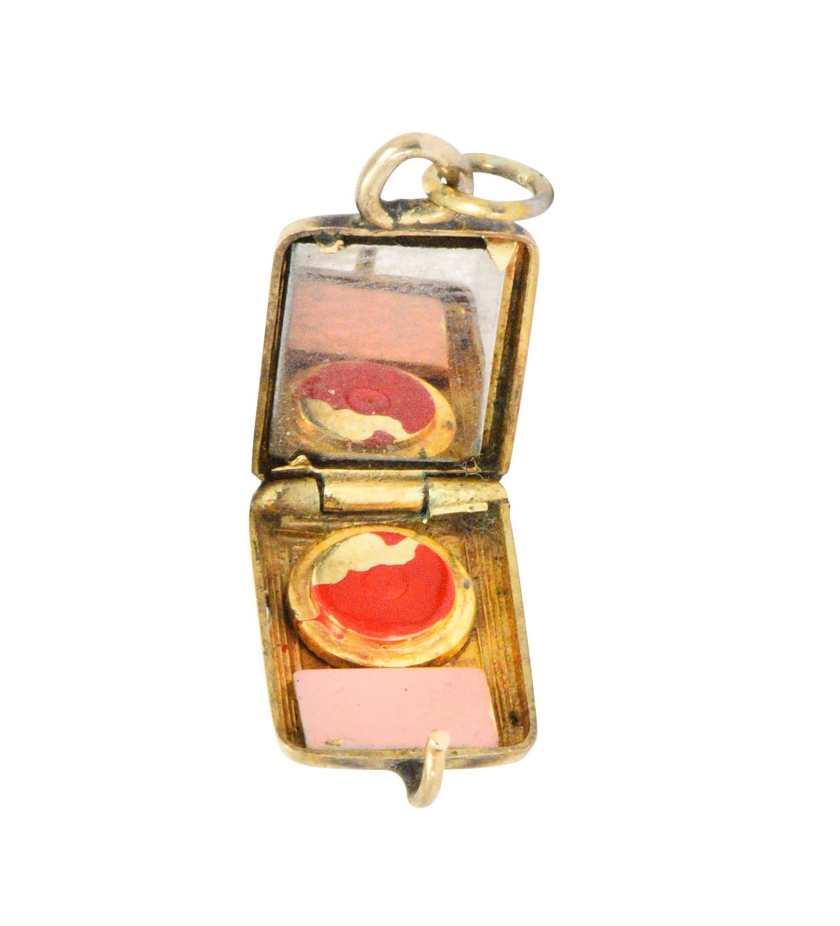 Designed as a cushion shaped makeup compact with deeply engraved striations

Opens on a hinge to reveal a mirror, a pink enamel puff, and red enamel rouge 

Exhibits loss; consistent with age, wear, and use

Completed by a jump ring bale

Stamped
