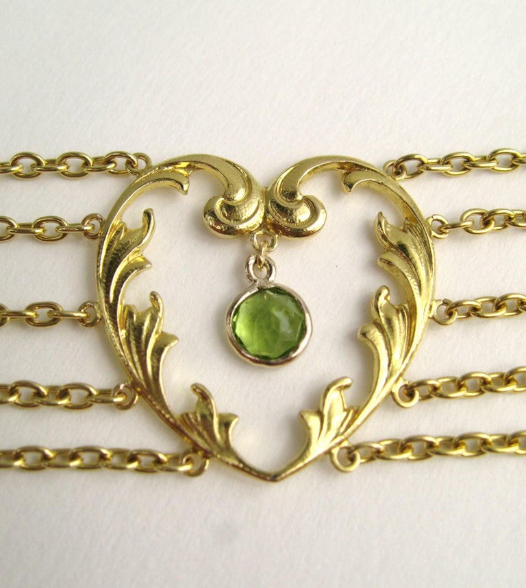 Stunning art nouveau choker, with a heart motif. 5 strands of chain connecting each heart. Bezel set dangling peridots stones in each. The necklace measures 13.5” end to end x 7/8