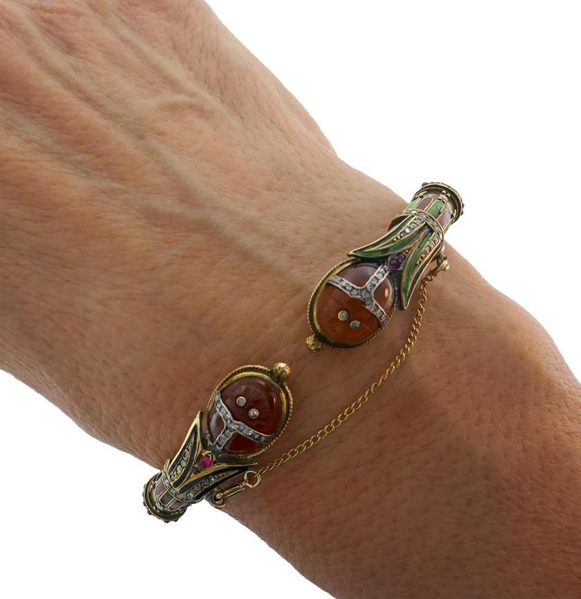 Colorful bracelet created in the 1910s and inspired by Egyptian Revival motifs. 
Made of 14 karat yellow gold, the bangle features two carved carnelian scarabs and accented with rose cut diamonds, ruby and enamel. 
Measurements: 6-3/4 x 3/4 inches
