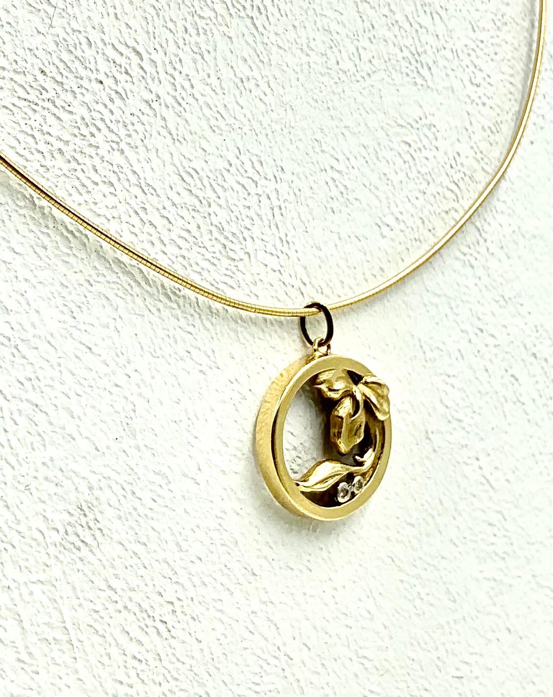 Lovely Art Nouveau 14K yellow gold and diamond pendant, a gold iris within a circle with two diamonds depicting drops of dew. Textured and polished gold finish.
Marks: 14K, makers mark