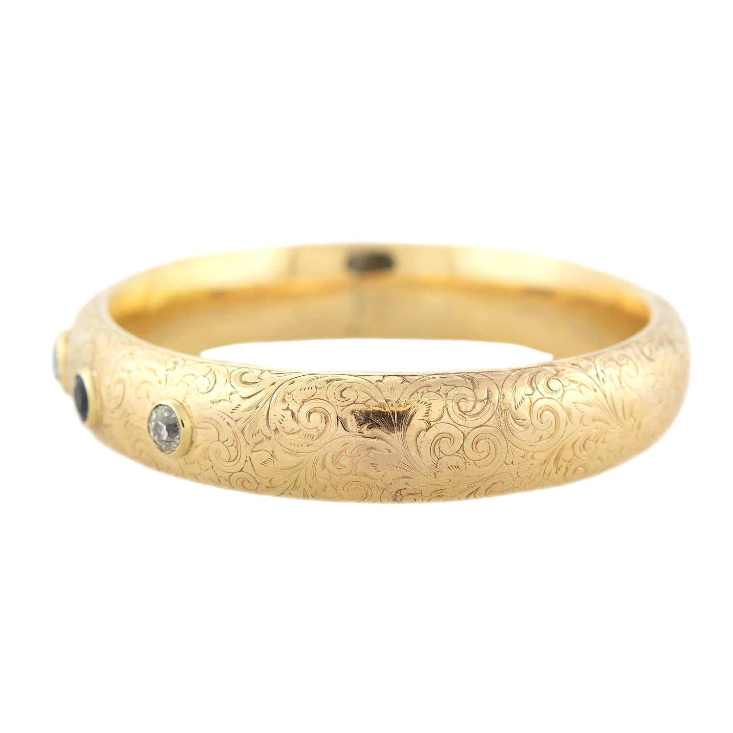 A stunning bangle bracelet from the Art Nouveau (ca1900s) era! Crafted in vibrant 14kt yellow gold, this highly polished bracelet is adorned by five bezel-set gemstones. Three Old Mine Cut diamonds and two rich blue sapphires grace the surface in