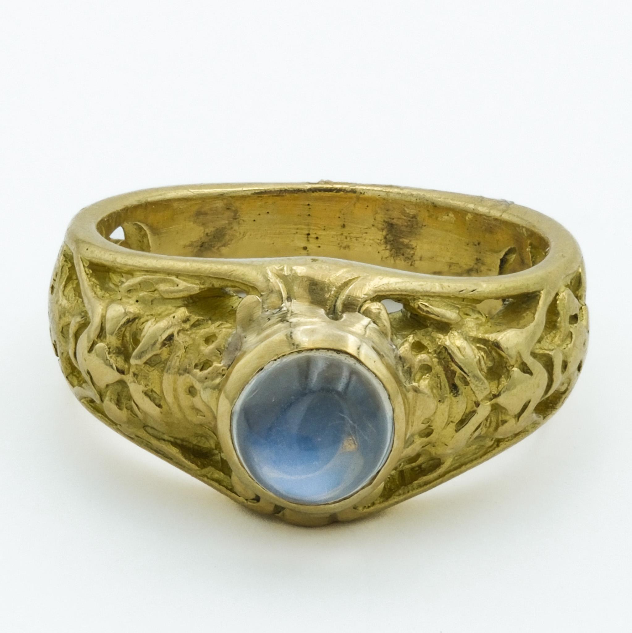 This is an exquisite piece of Art Nouveau jewelry, specifically an 18-karat gold ring that encapsulates the era's affinity for organic and flowing designs. The band of the ring features intricately carved figure that suggest a baroque influence,