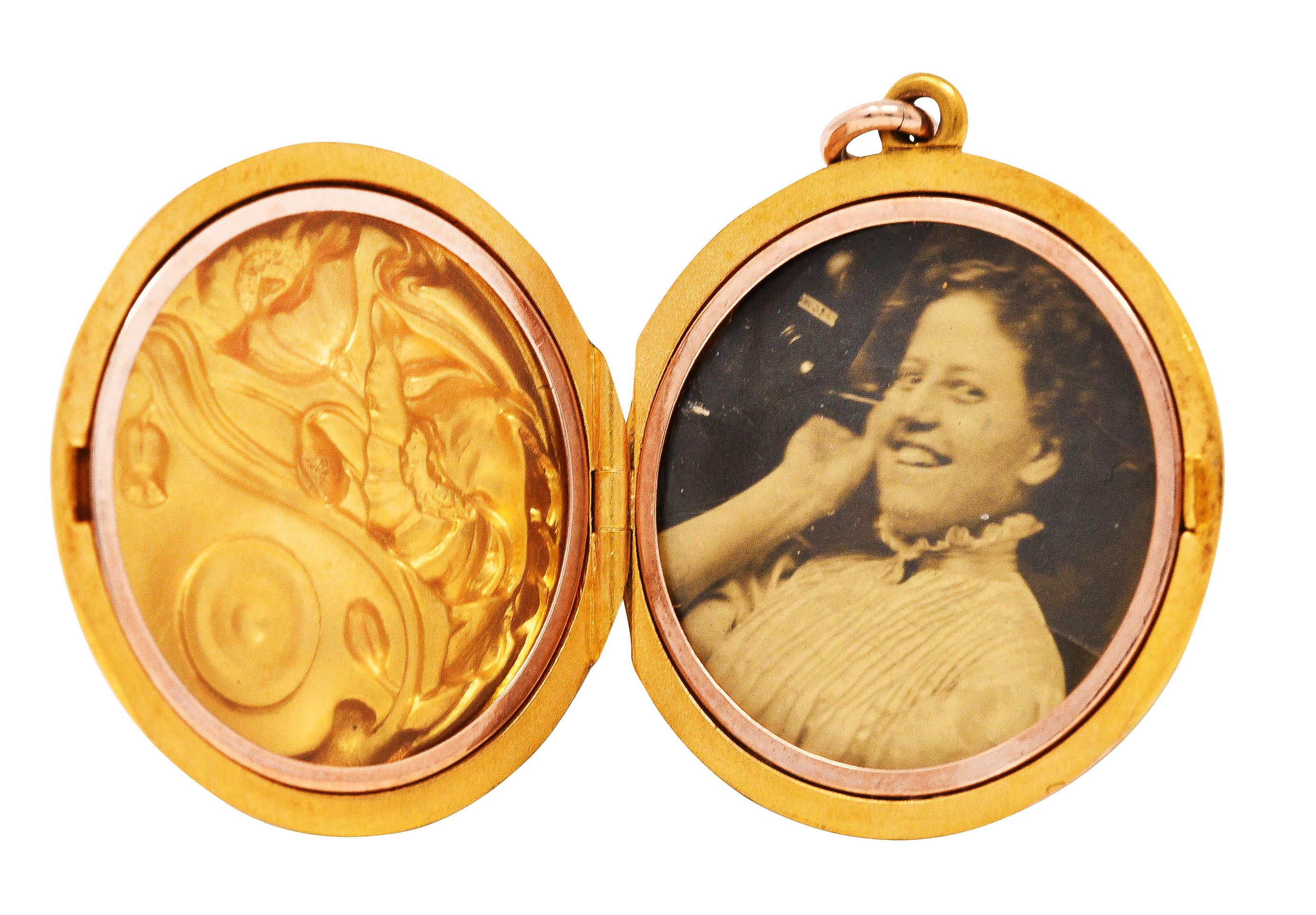 Circular locket features a repoussè rendering of stylized florals

Opens on a hinge to reveal two circular recesses with removable plastic covers

One side features a sepia portrait of a smiling Edwardian woman

Tested as 18 karat gold

Circa: