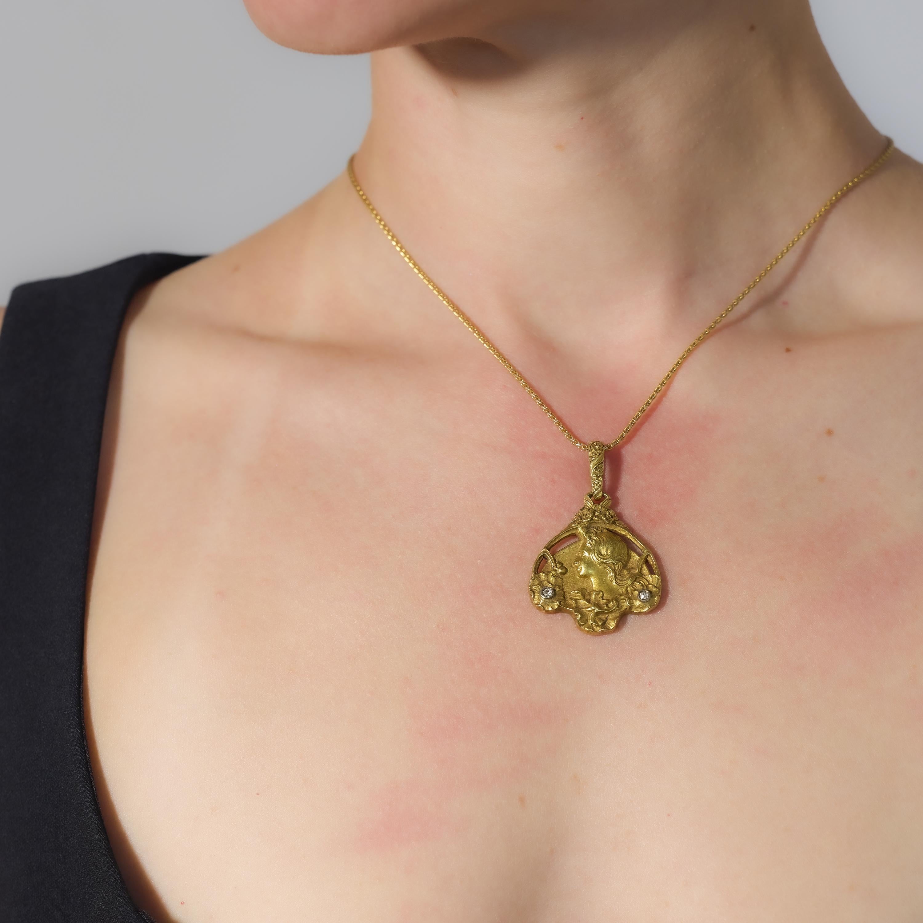 Ce gracieux collier Art nouveau présente un pendentif fluide de 2 x 1,25 pouces orné de deux délicats diamants taille unique, d'une valeur totale d'environ 0,05 carat. Réalisée en or jaune 18 carats et suspendue à une chaîne complémentaire en or