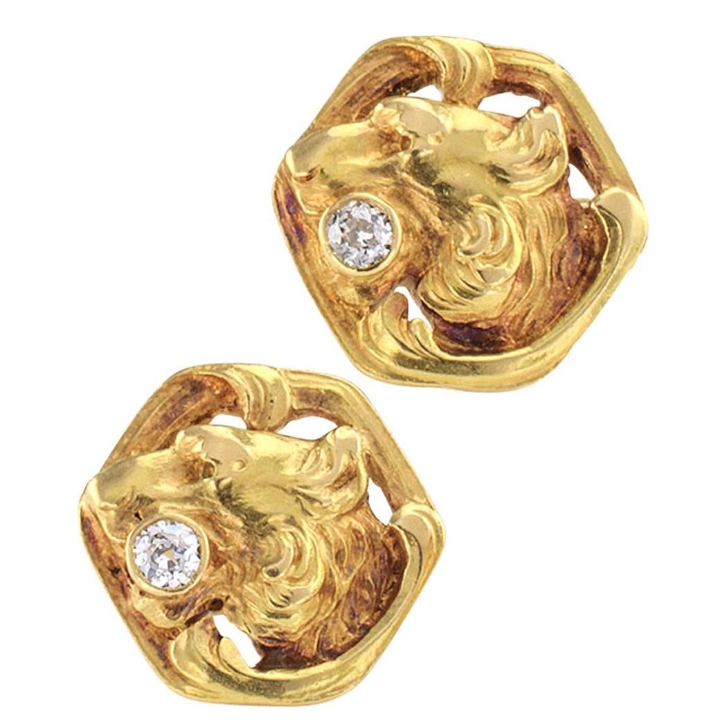 Art Nouveau 1905 lion head cufflinks with diamonds and gold. The faces of these matching, open work designs feature, in relief, the profile of a ferocious lion with a bezel-set round diamond in the grip of its fangs, all framed by organic motifs,