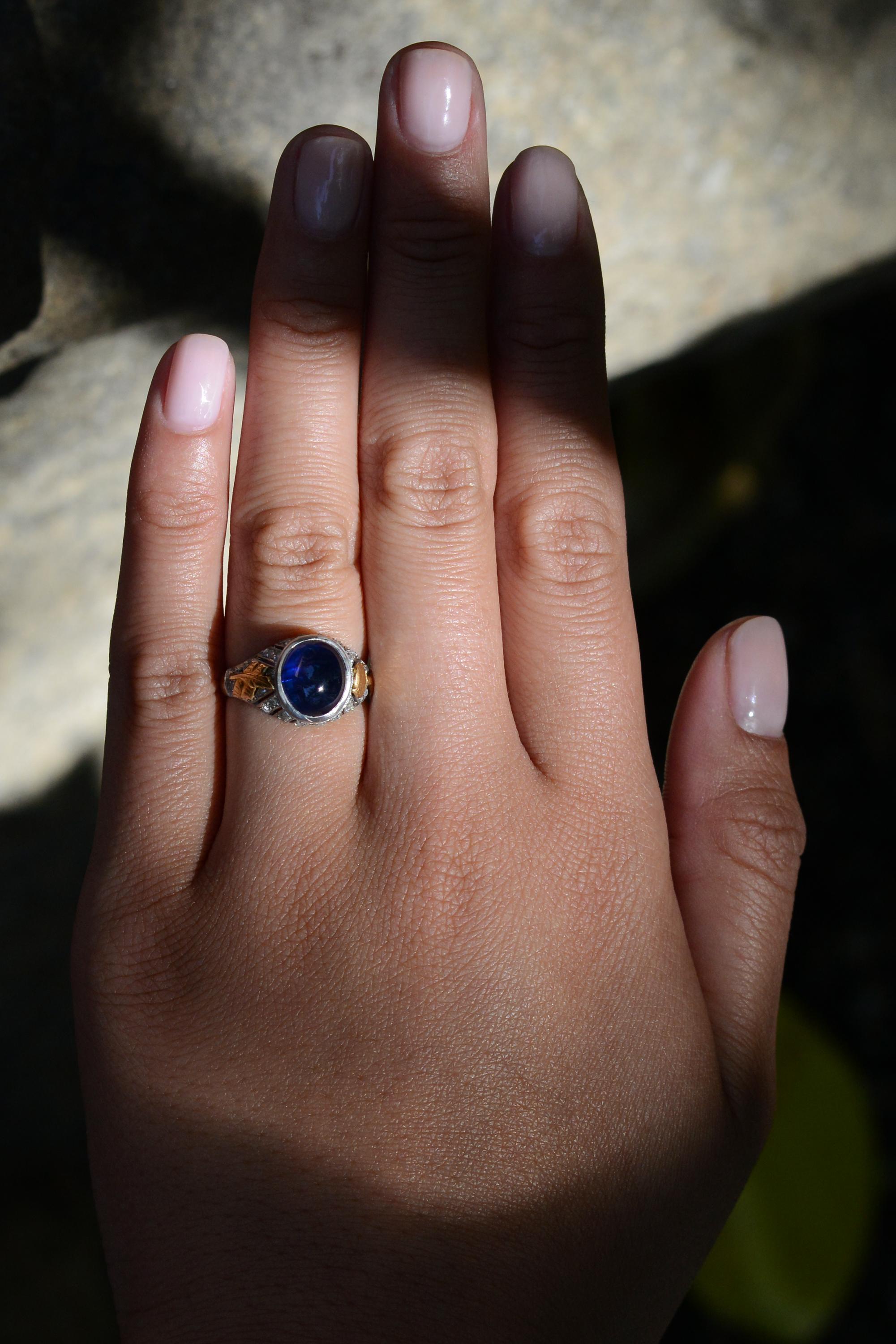 This antique Art Nouveau gemstone engagement ring presents a lovely 2 tone composition centered with a dark blue sapphire cabochon. Crafted with exquisite attention to detail, the romantic rose cut diamonds perfectly complement the tranquil natural