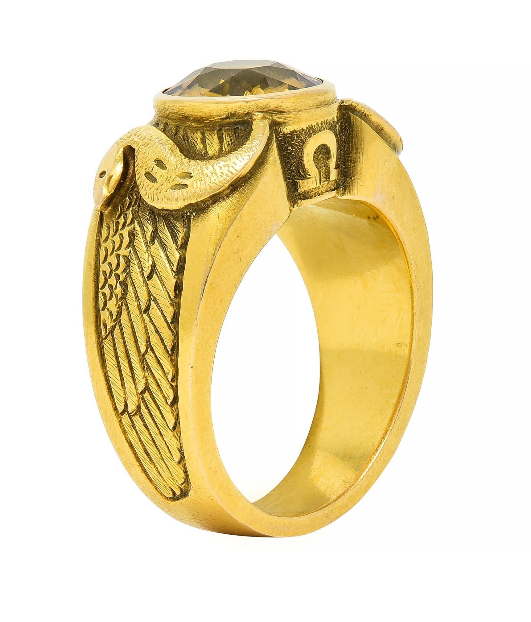 Centering a cushion cut zircon weighing approximately 4.57 carats - transparent medium brownish yellow 
Bezel set and flanked by engraved wing motif sweeping down shoulders 
With raised curling serpents and accented by omega symbol profiles 
Stamped