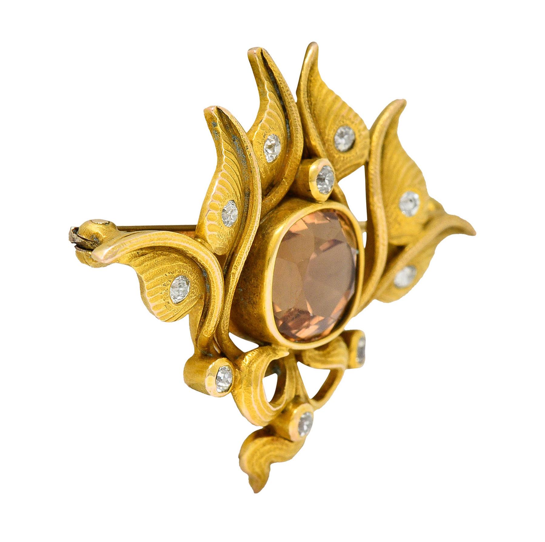 Brooch is designed as meandering whiplashed foliate

Centering a mixed cushion cut imperial topaz weighing approximately 4.75 carats

Transparent with medium light with strong pinkish orange color
 
Surrounded by old European cut diamonds weighing