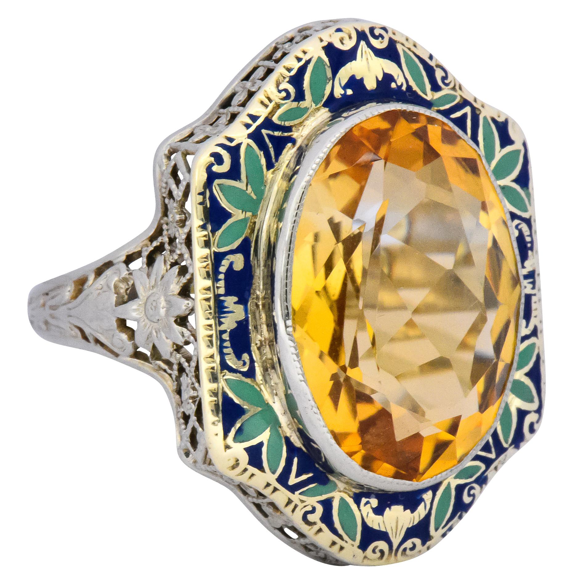 Centering an oval cut citrine weighing approximately 6.15 carats, bright orangey yellow

Bezel set with a blue and green enamel foliate motif surround

With a pierced floral and lattice-work white gold gallery

Stamped 14K

Ring Size: 6 3/4 &