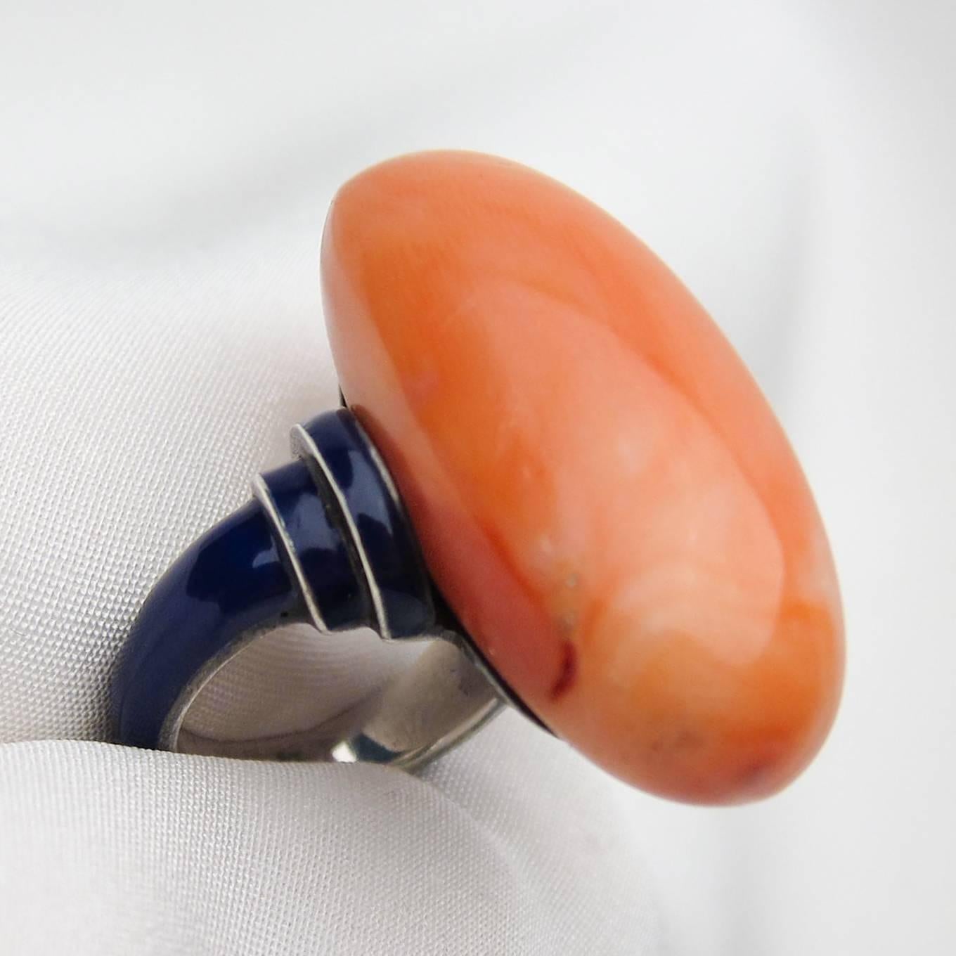 Circa 1910. This fabulous antique cocktail ring features an astounding 85 carat, oval cabochon-cut orange coral stone accented by a deep-blue enamel and silver setting. This handmade ring is a crazy cool statement piece!!