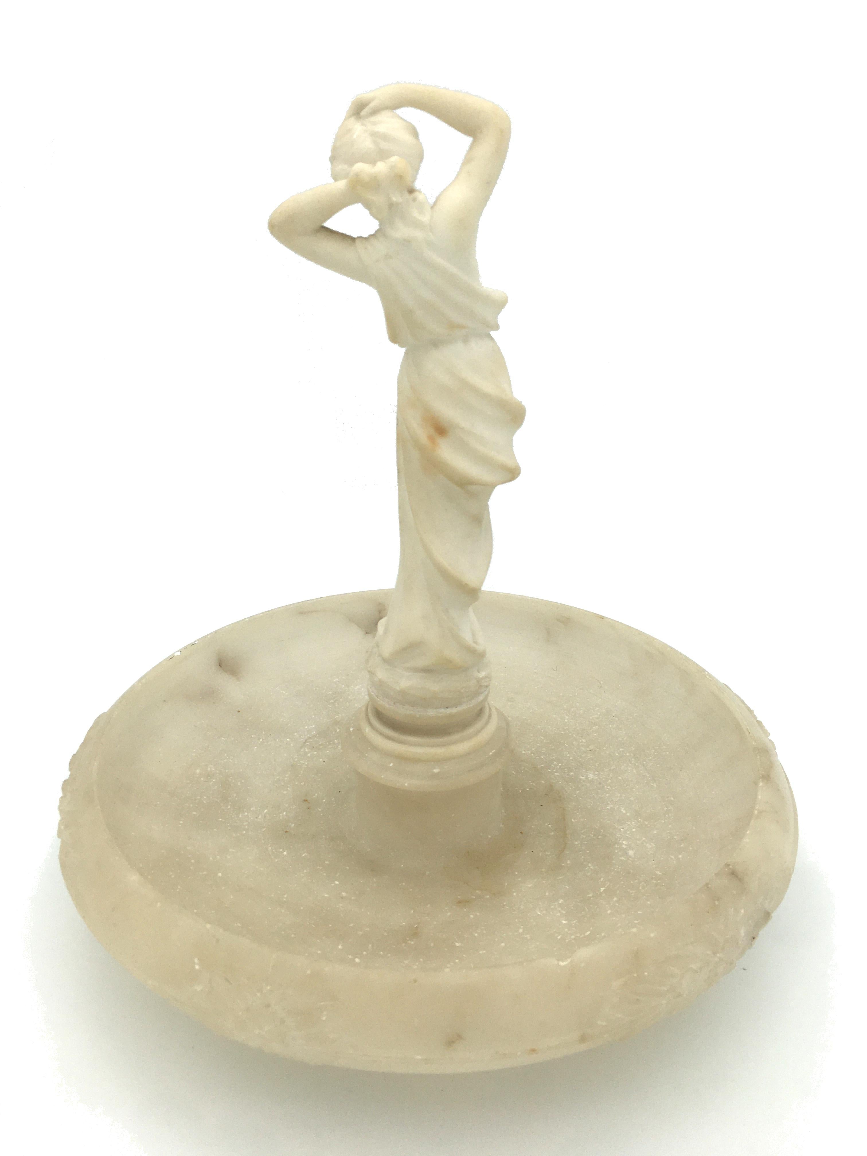 Delightful Art Nouveau alabaster vide-poche with a Venus statue, treated like a miniature fountain. The venus that is draped Roman-style has a bare breast and fixes her hair with her hands. The basin of the vide-poche, the rim of which is decorated