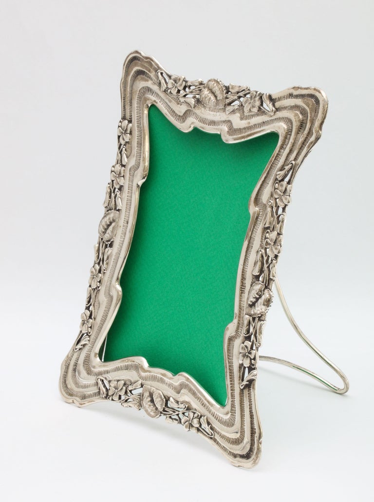 Art Nouveau, all sterling silver picture frame, The Theodore B. Starr Co., New York, circa 1895-1900. Hinged easel of frame is also sterling silver. Measures 7 3/4 inches high at highest point x 6 inches wide at widest point x 6 inches deep when