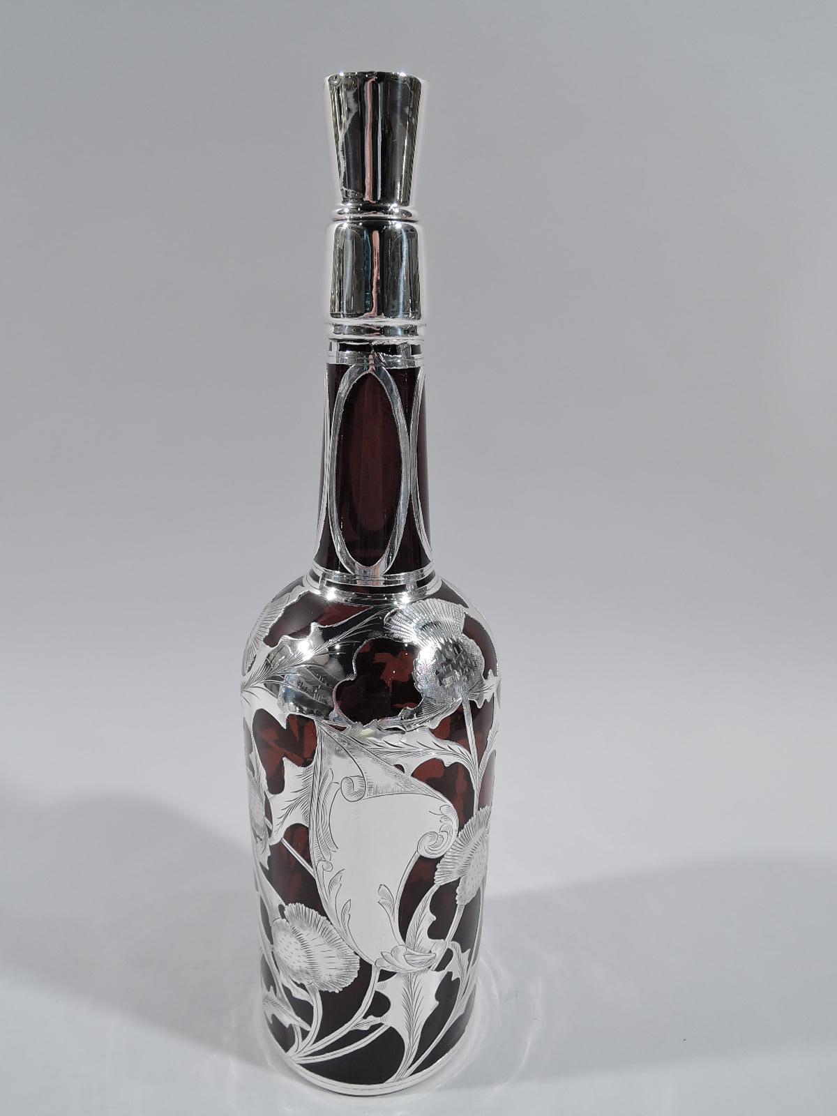 Turn-of-the-century Art Nouveau amber glass bottle decanter with engraved silver overlay. Traditional cylindrical form with sloping shoulder and upward tapering neck. Open and interlaced overlay with thistle motif and asymmetrical strapwork