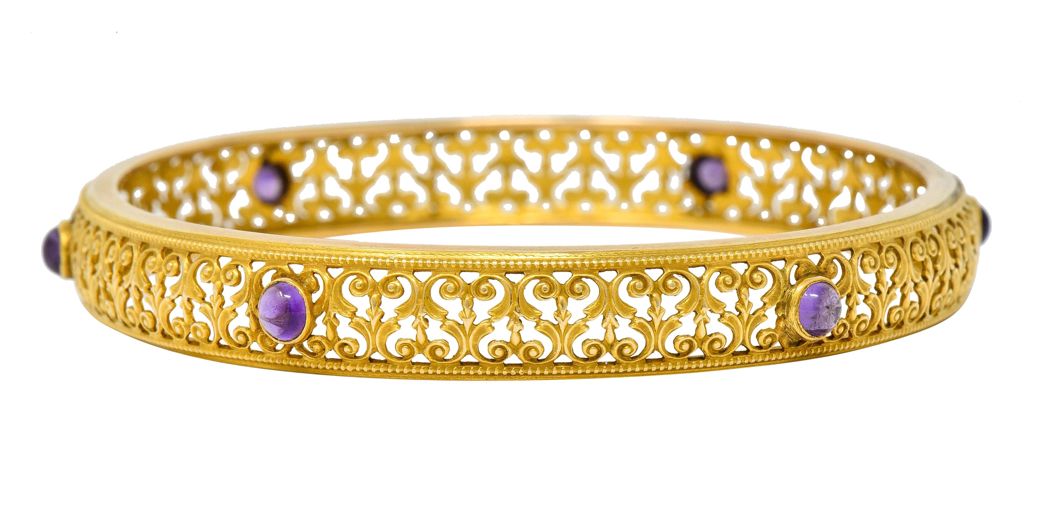 Bangle style bracelet with milgrain edges and a pierced scrolled filigree design

Accented by bezel set round amethyst cabochon measuring approximately 3.5 mm

Very well-matched medium-light purple in color

Tested as 14 karat gold

Circa: