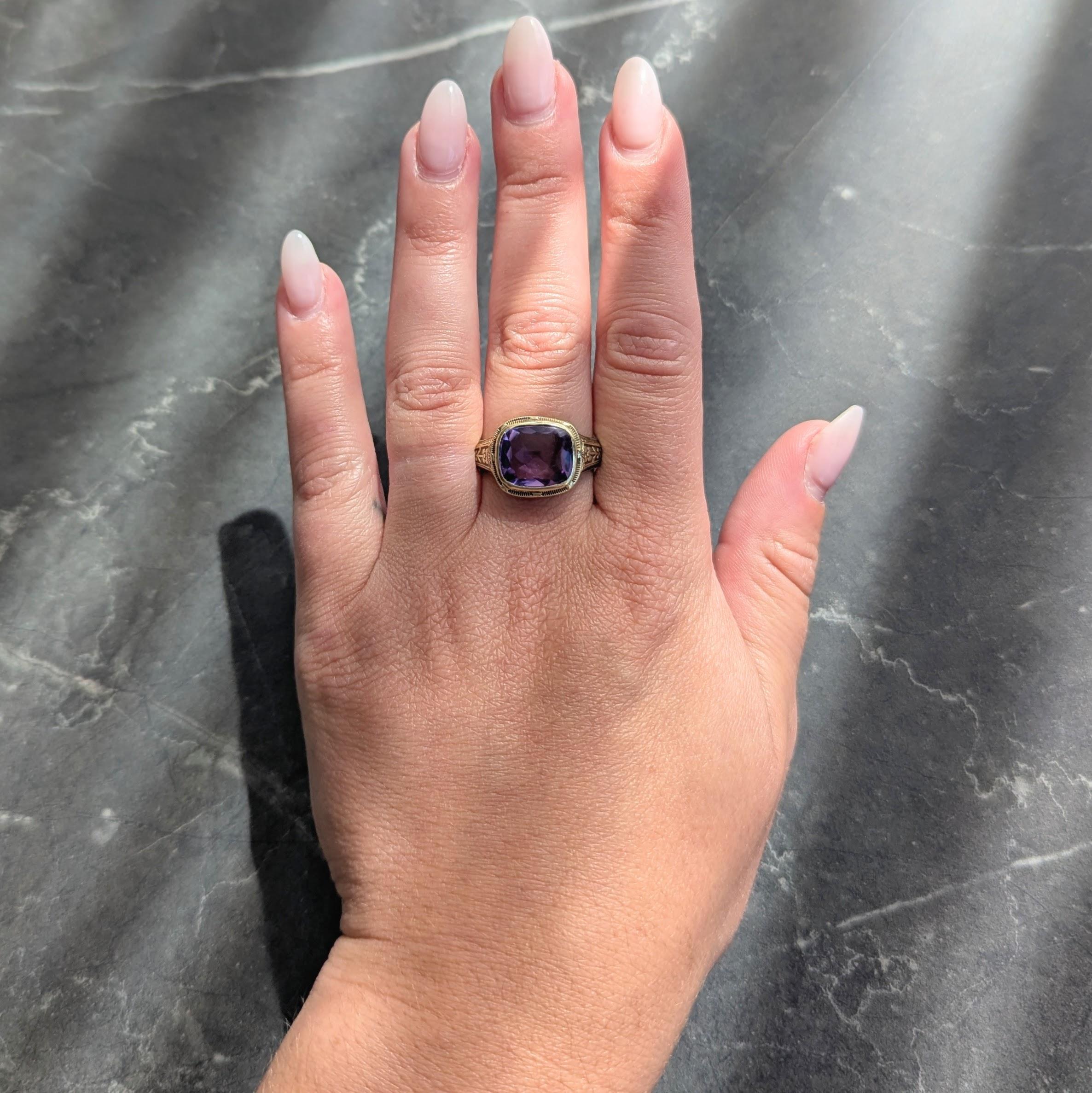 Al centro, un'ametista a forma di cuscino con un top a scaglie e sfaccettature a scacchiera di 10,0 x 12,0 mm.
Colore viola medio trasparente con saturazione media - incastonato in una lunetta scanalata
Fiancheggiato da spalle scanalate con motivo