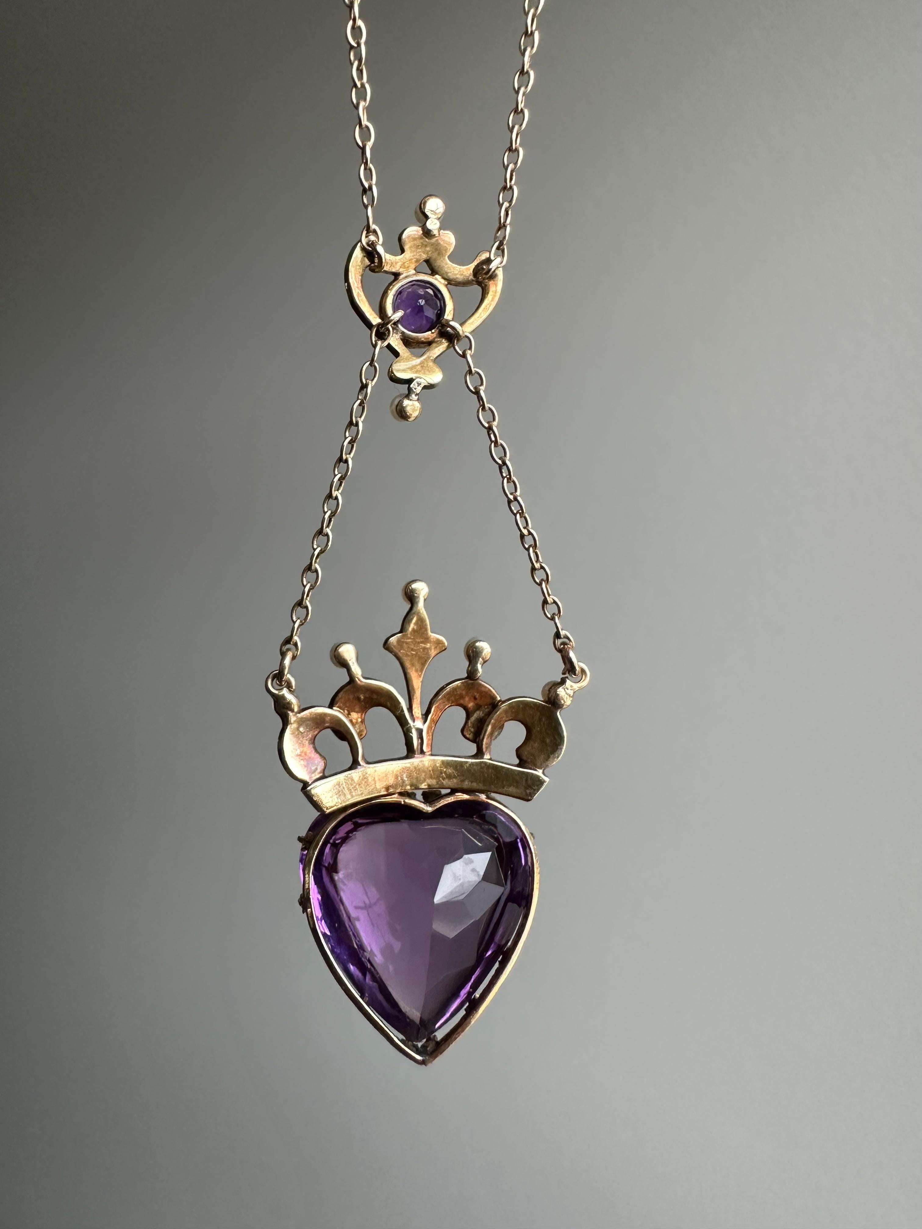 Dating to the turn of the 20th century, this enchanting crowned heart necklace displays a regal buff-top amethyst heart surmounted by a delicate golden crown embellished by lustrous seed pearls. The heart is gracefully suspended by a tiny urn