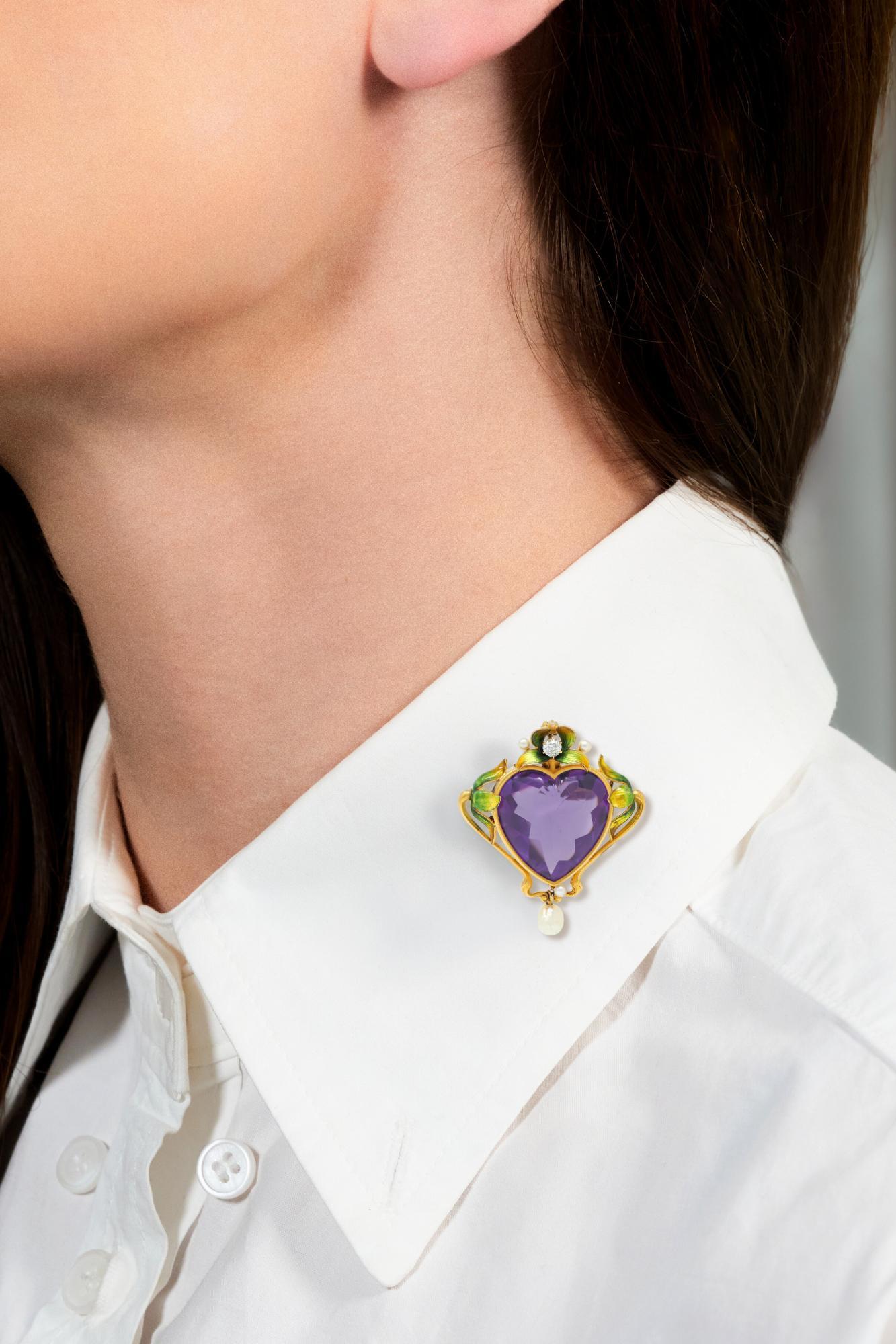 Zentrierung eines Amethysten im Herzschliff mit Buff-Top - 18,5 x 18,5 mm groß
Transparentes mittleres Violett - Lünette mit peitschenförmigem Blattbesatz
Mit einem Diamanten im alten Minenschliff von etwa 0,12 Karat
Augenrein und glänzend -