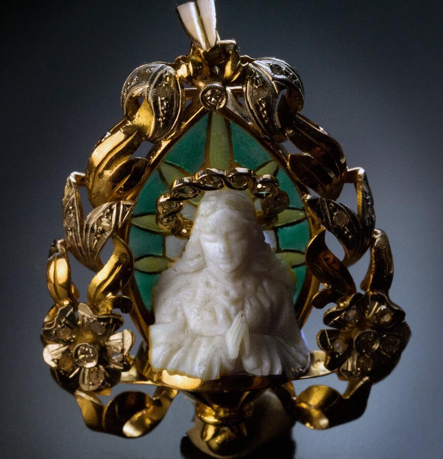 Spanish or French, circa 1910.
Placed inside a platinum and 18K gold floral motif frame, is an intricately carved miniature bone bust of Madonna with a platinum-topped gold halo embellished with rose-cut diamonds.
The depiction of Madonna is set