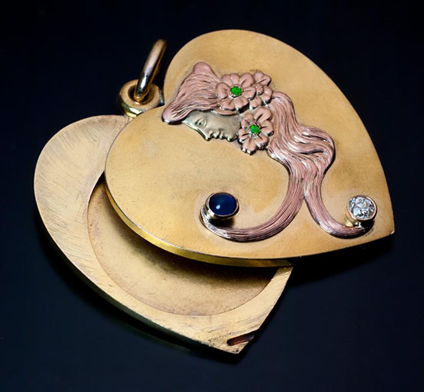 made in Moscow between 1899 and 1908
 The 14K three-color gold heart locket features a female face profile (green gold) with flowing hair (rose gold) embellished with a cabochon cut sapphire,
 an old European cut diamond (approximately 0.20 ct) and