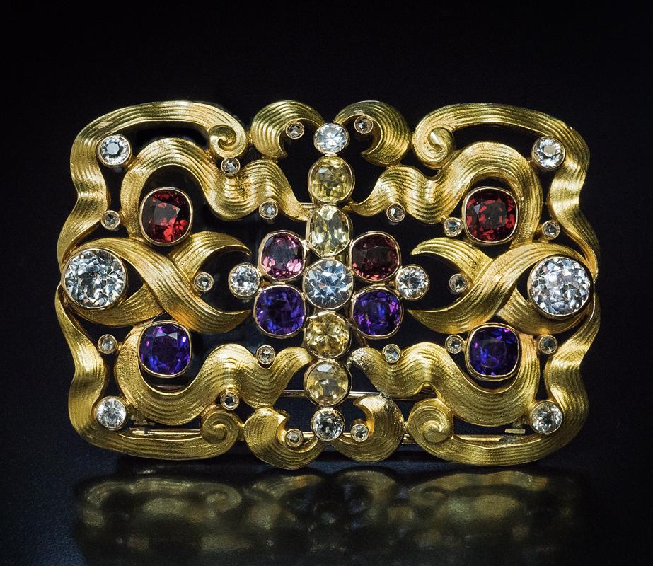 Made in Moscow between 1899 and 1908.

This unique, one of a kind, 14K gold Art Nouveau belt buckle / brooch is designed as interlacing ribbons accented by bezel-set white sapphires, Siberian amethysts, almandine and rhodolite garnets, aquamarines,