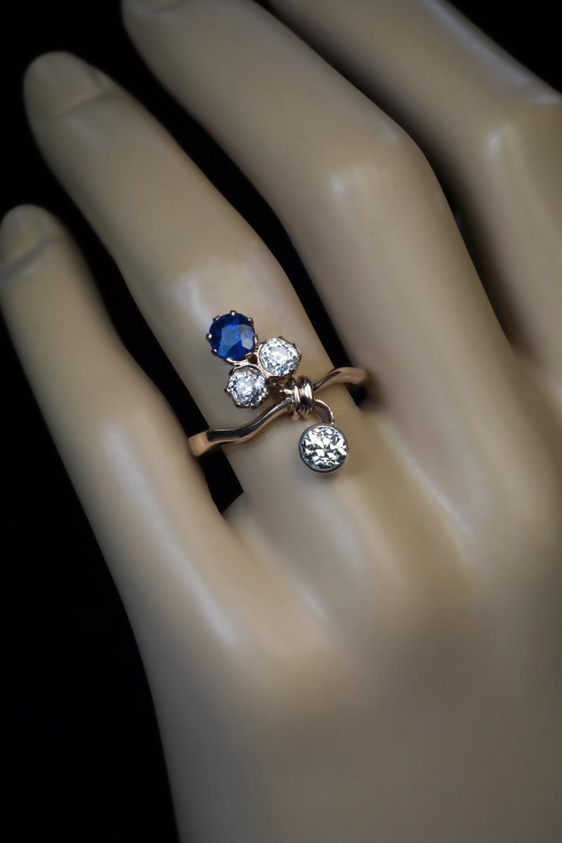 Russian, circa 1900.

The 14K gold ring is designed in Art Nouveau taste as a stylized ribbon-tied flower embellished with a very fine blue sapphire and three chunky old mine cut diamonds.
The sapphire measures 5 x 3.6 mm and is approximately 0.65