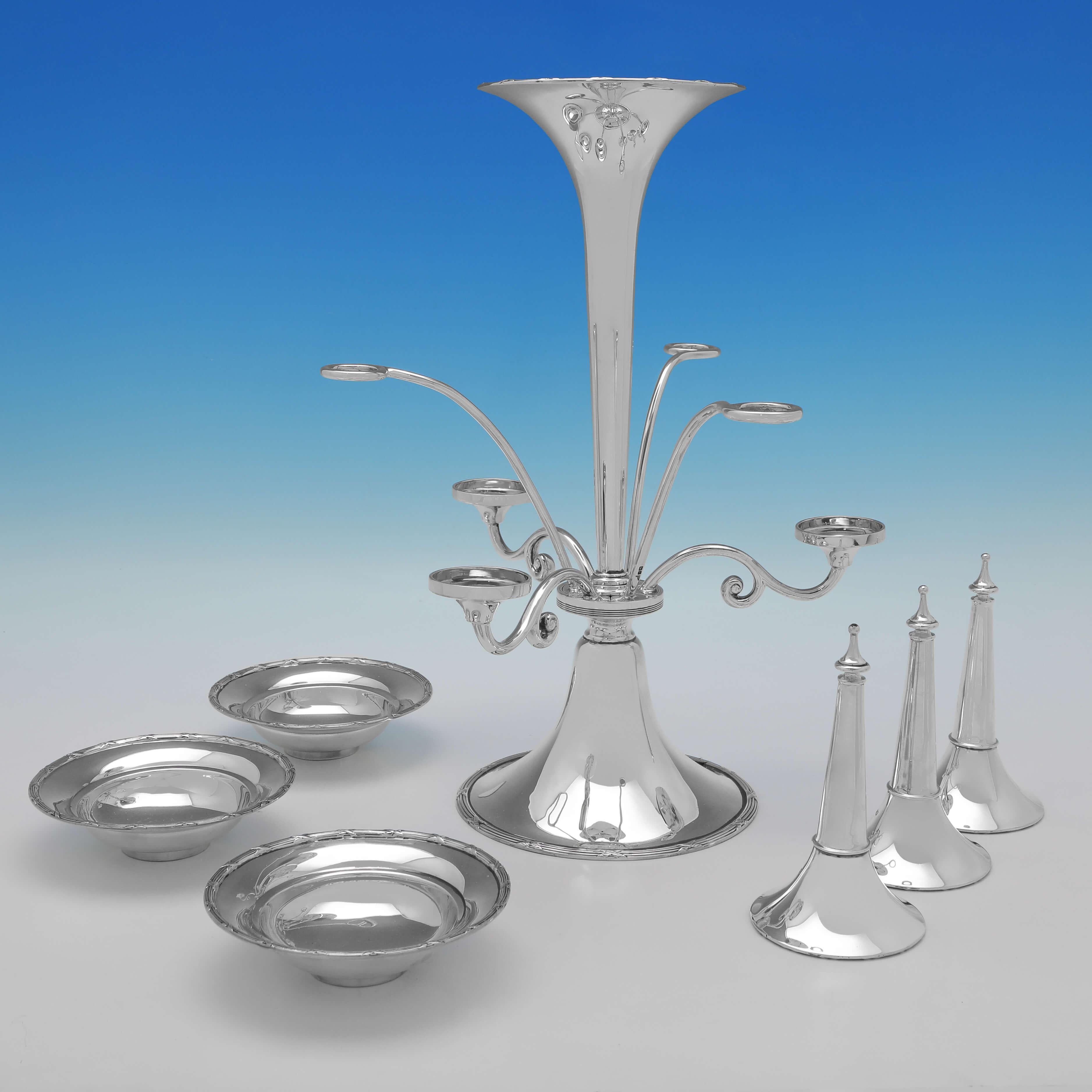 Hallmarked in Sheffield in 1910 by Walker & Hall, this charming, Antique Sterling Silver Epergne, has three side dishes, three smaller side vases and a larger central vase for flowers. 

The epergne measures 15