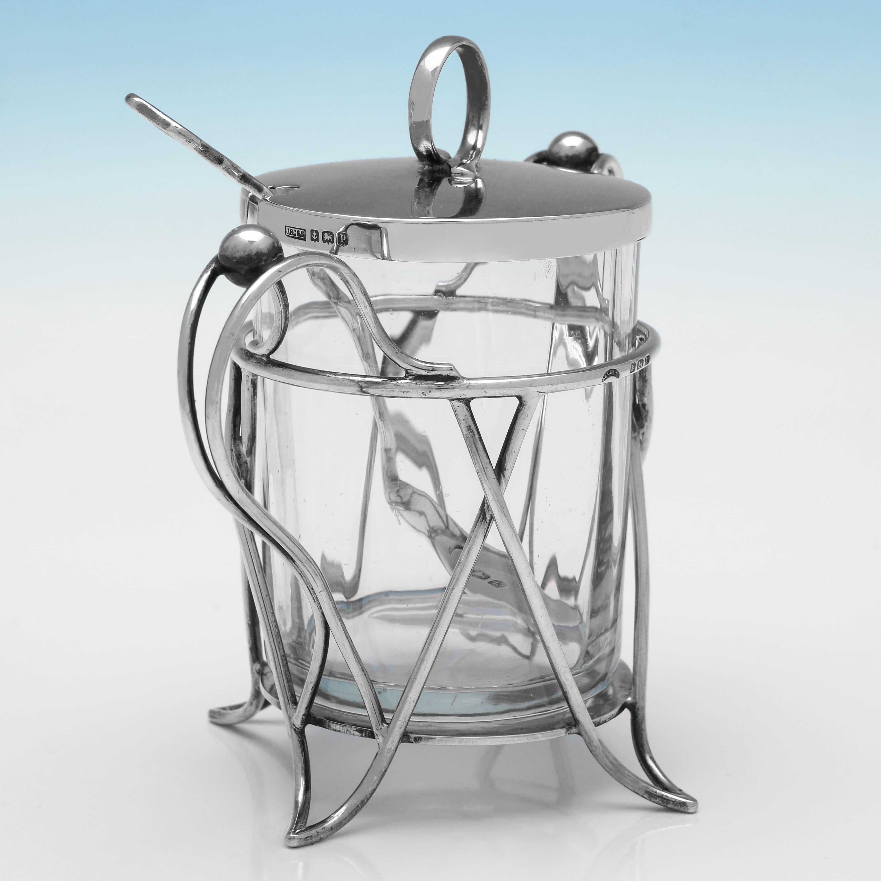 Hallmarked in Birmingham in 1909 by J. B. Chatterley & Sons Ltd., this charming, Antique, Edwardian Sterling Silver & Glass Jam Pot, is in the art nouveau taste, with sweeping handles, and a twisted stem spoon. The jam pot measures 5.25