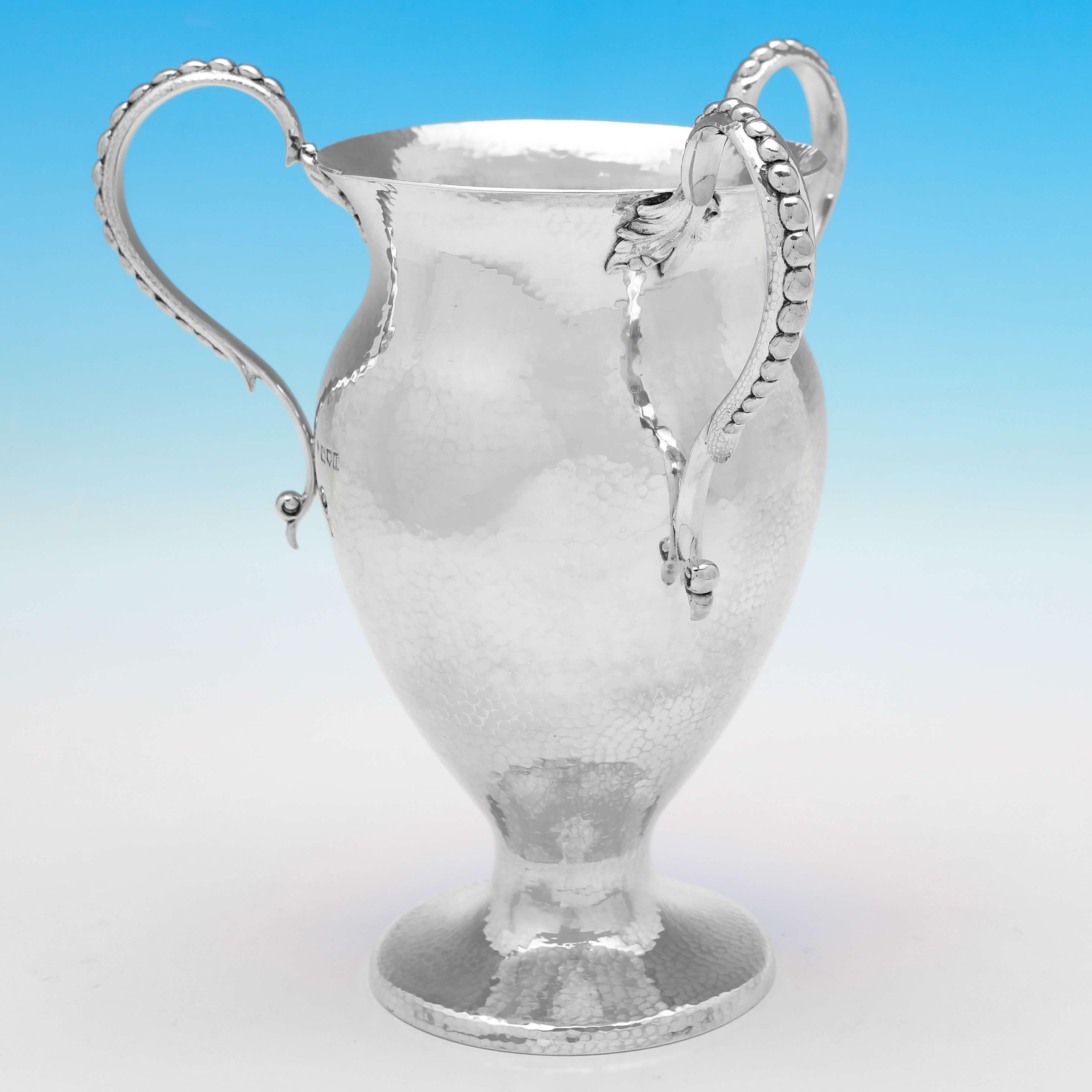 Hallmarked in London in 1910 by Holland, Aldwinckle & Slater, this stylish, Antique Sterling Silver Three-handled Cup or Tyg, is in the Art Nouveau taste, with a hammered finish, and vacant cartouche to one side. 

The cup measures 10