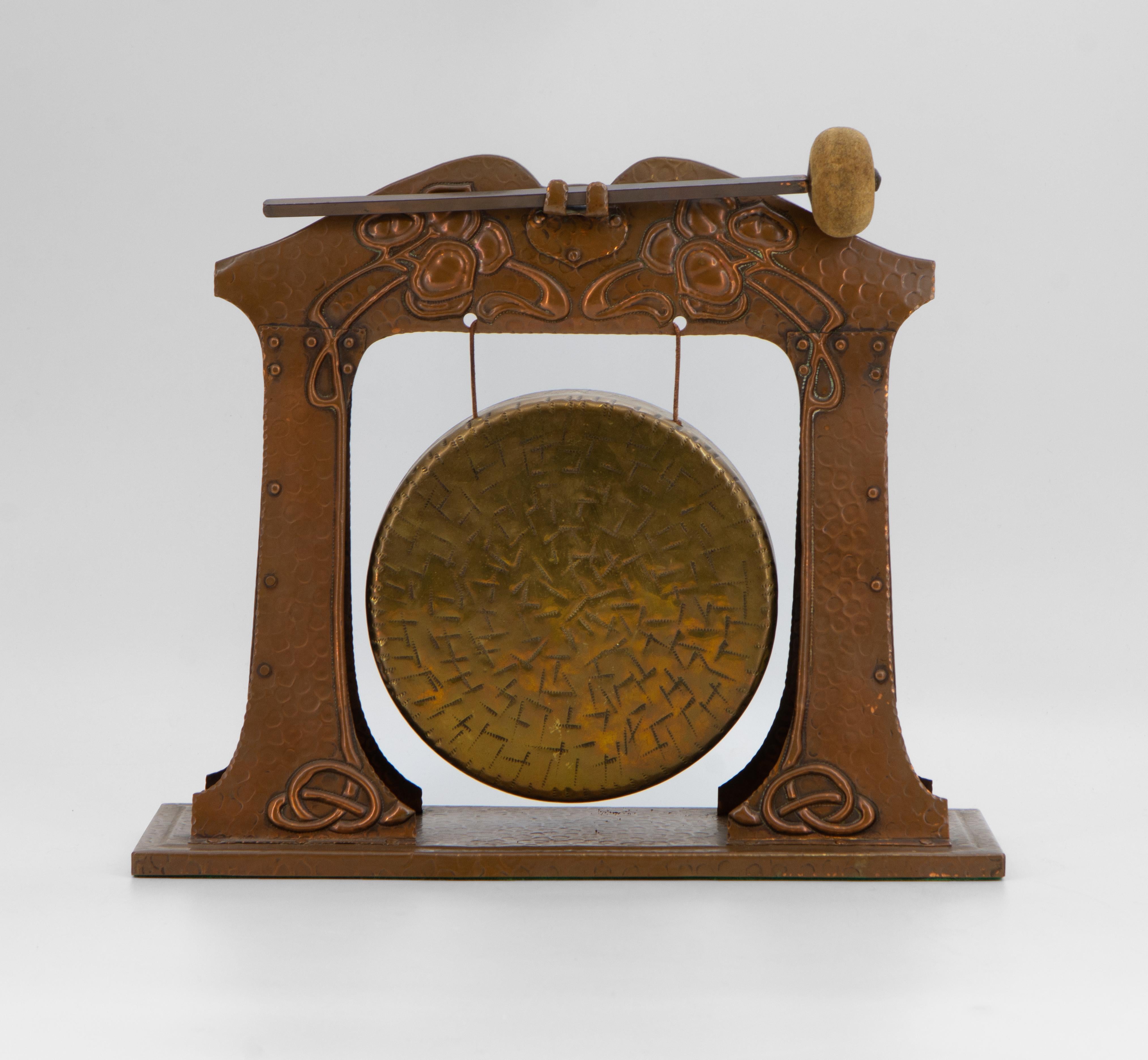 An Art Nouveau copper and brass table top dinner gong. Circa 1910.

The brass gong is suspended from the copper stand embossed with sinuous stylized flower design. It has a lovely resonant ring when struck by the original copper-handled