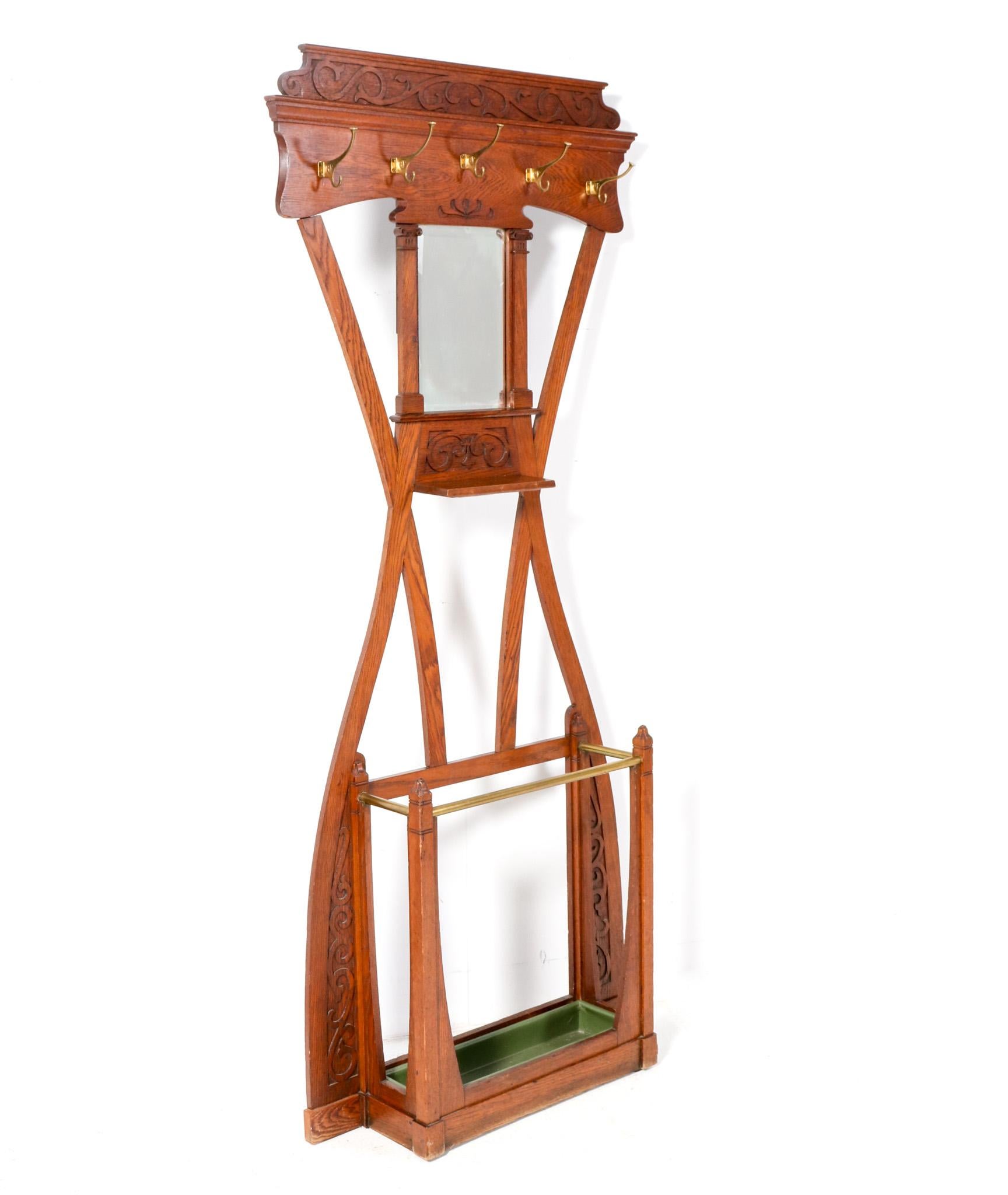 Stunning and rare Art Nouveau Arts & Crafts hall tree or porte manteau.
Striking Dutch design from the 1900s.
Solid oak frame with five original patinated brass hooks and integrated umbrella stand.
Original beveled mirror and hard-carved