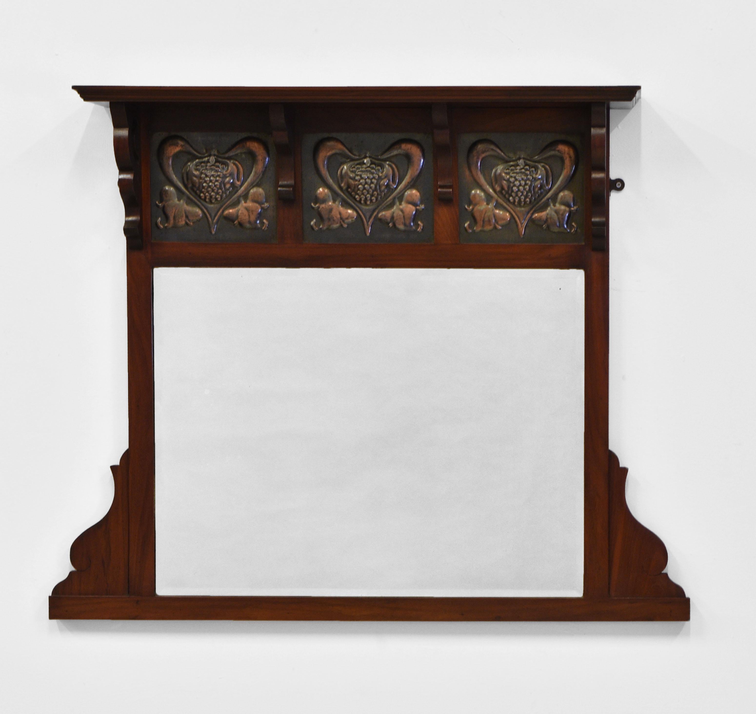 An Art Nouveau walnut over mantle wall mirror, with sinuous metal heart shaped floral design insets, and pierced end brackets. British - Circa 1900.

It is in very good condition for its age, with the original bevelled glass. There is no damage to