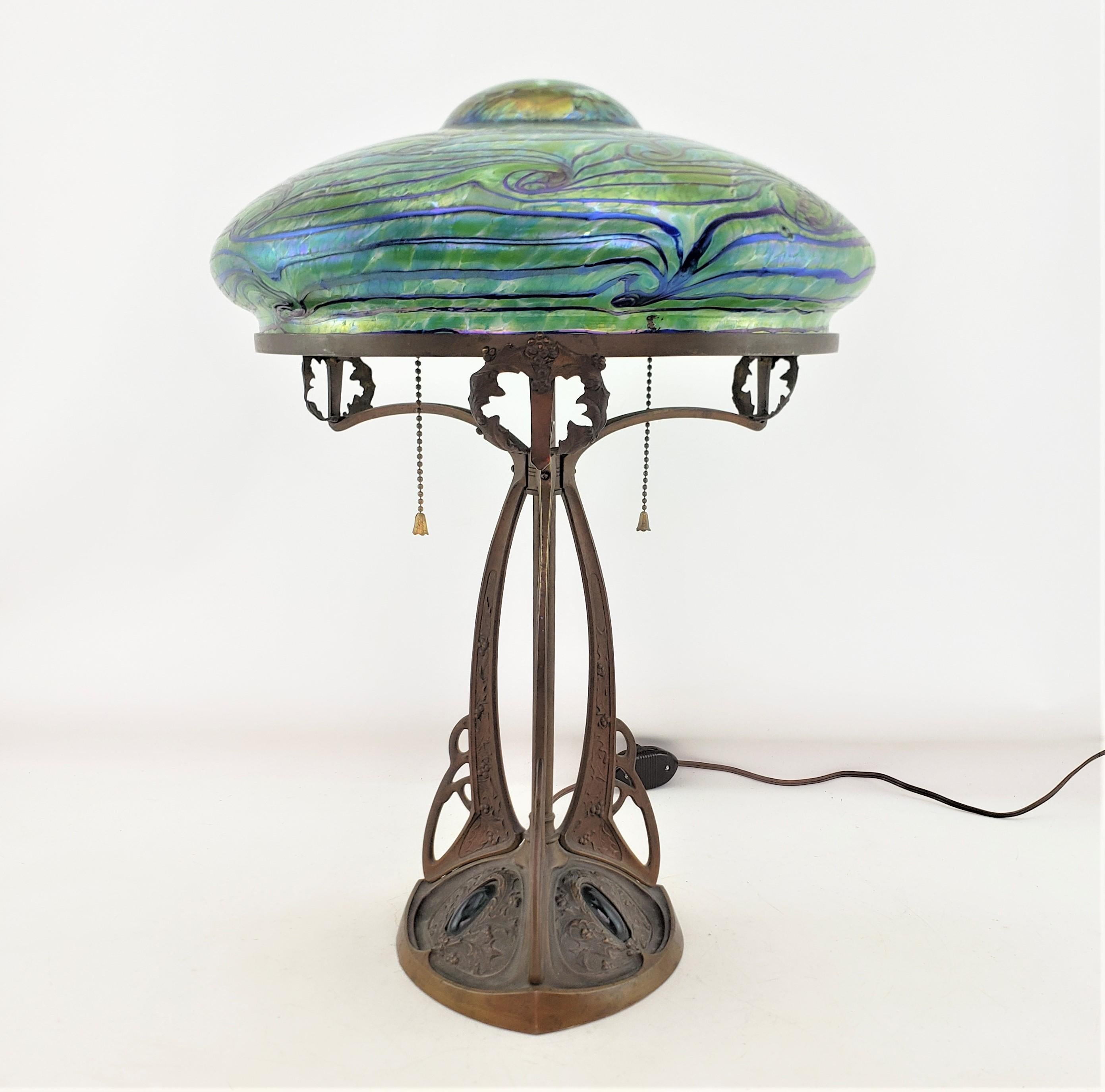 Diese antike Tischlampe ist unsigniert, stammt aber vermutlich aus Österreich und wurde um 1900 im Jugendstil gefertigt. Der Lampensockel besteht aus gegossener und patinierter Bronze mit einem stilisierten dreieckigen Sockel mit floralem Dekor und